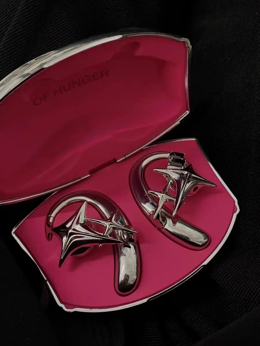 An open silver compact case with a hot pink interior displaying a pair of silver sculptural star-shaped ear cuff jewelry.