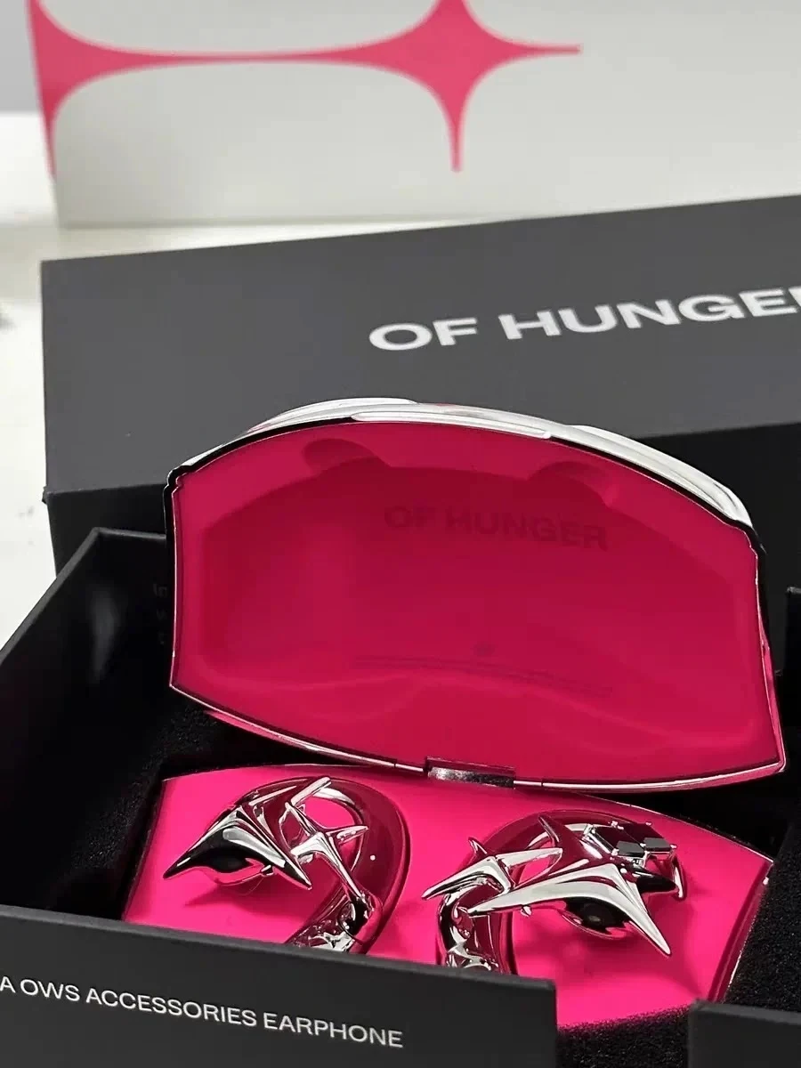 Metallic chrome ear accessory earphones in a spiked star design, displayed inside an open pink-lined charging case within black packaging labeled "OF HUNGER" and "A OWS ACCESSORIES EARPHONE".