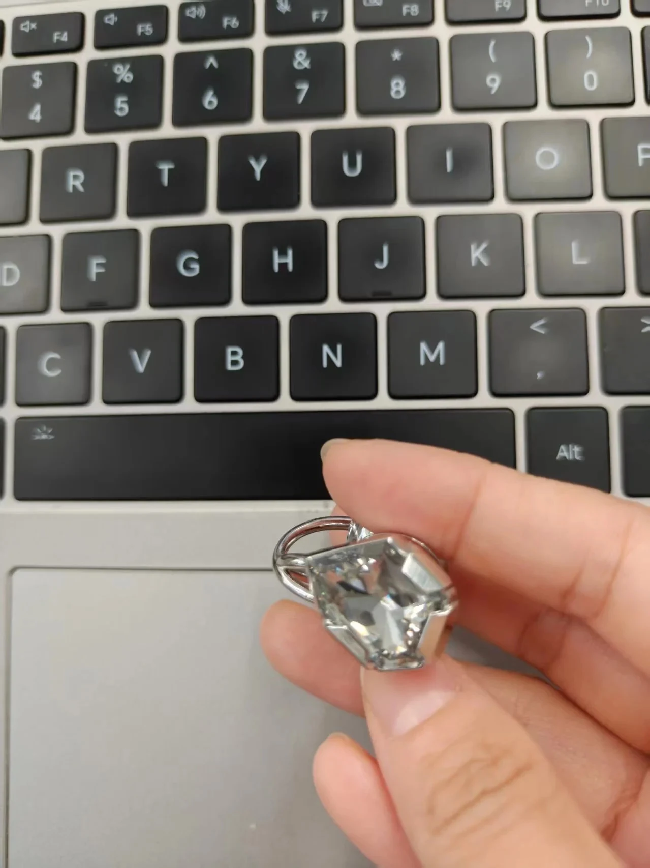 A hand holding a silver-tone clip-on earphone with a large faceted clear stone above a laptop keyboard.