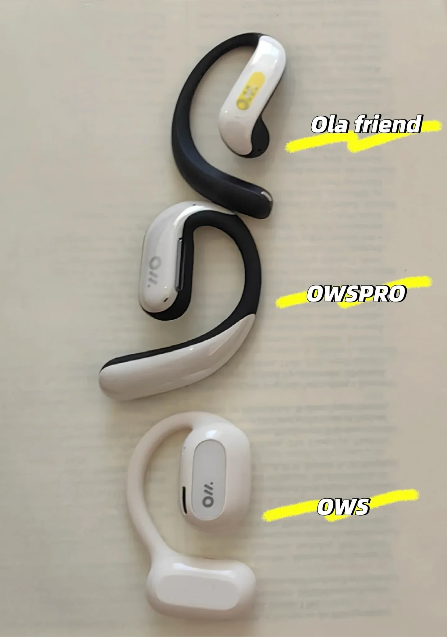 Three open-ear earphones arranged vertically on a flat surface to compare their shapes and sizes, labeled from top to bottom as Ola friend, OWSPRO, and OWS.