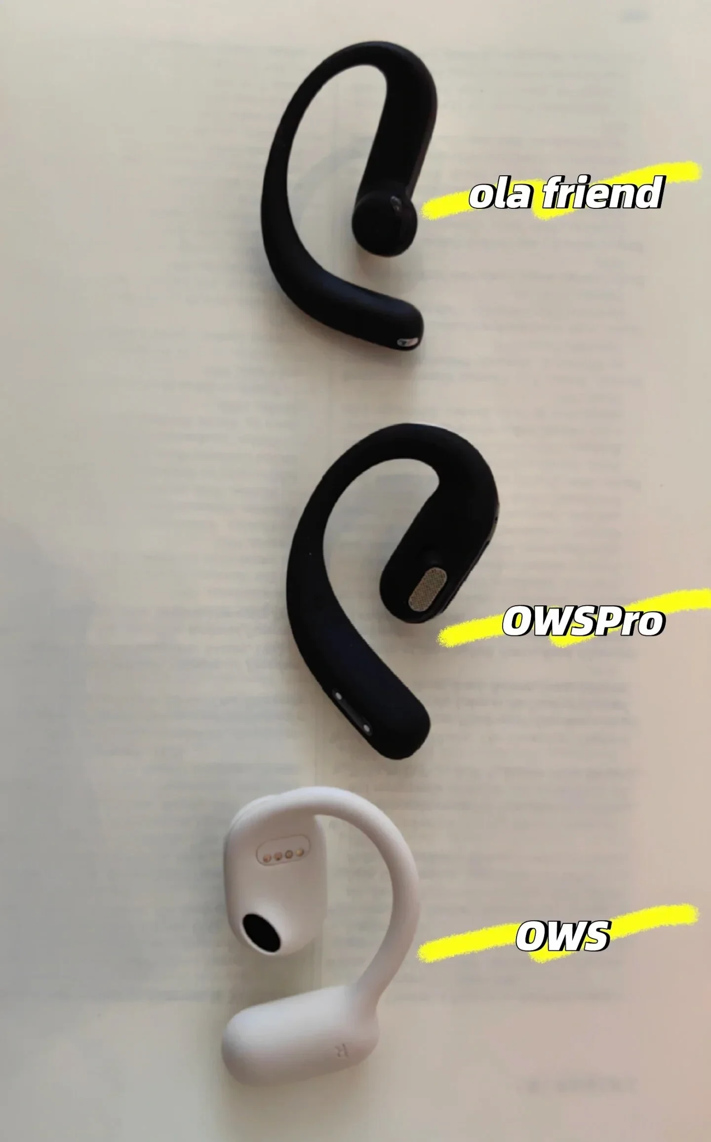 Three open-ear wireless earbuds arranged vertically on a white surface for comparison: a black ola friend at the top, a black OWSPro in the middle, and a white OWS at the bottom, each labeled with yellow highlighted text.