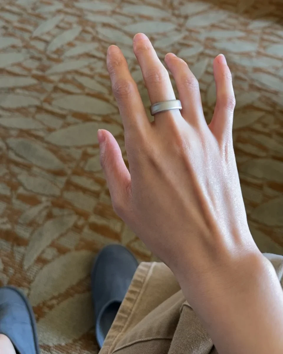 A person's hand wearing a matte silver smart ring on the middle finger.