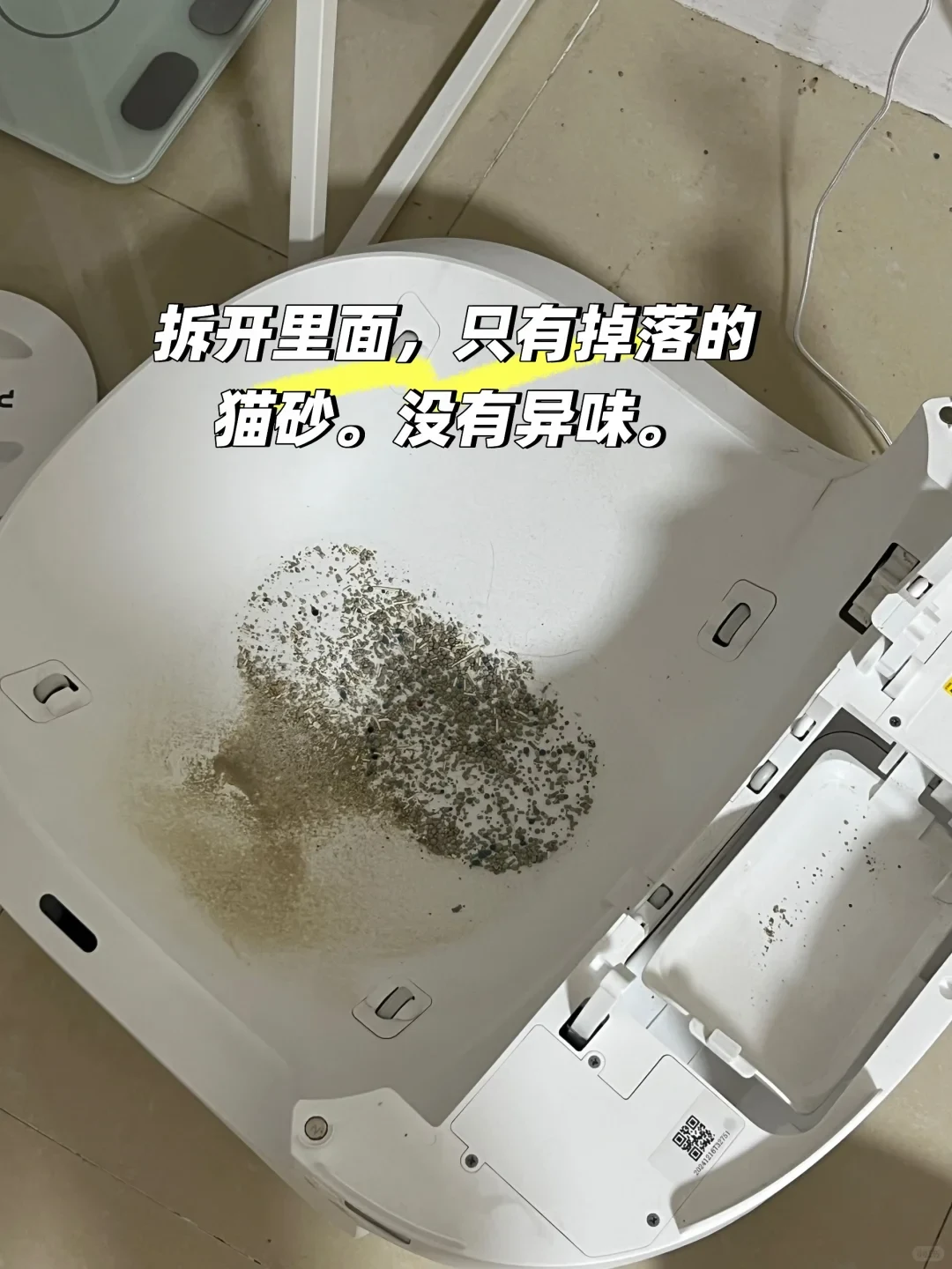 An overhead view of the opened interior base of a white automatic cat litter box, showing an accumulation of scattered cat litter granules and dust on the curved plastic floor.