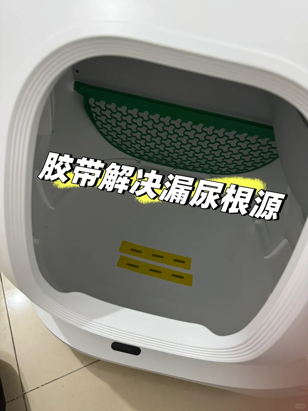 Interior view of a white hooded cat litter box showing a green sifting mesh at the top and two strips of yellow tape stuck over slots at the bottom, with Chinese text overlay describing a solution for urine leaking.