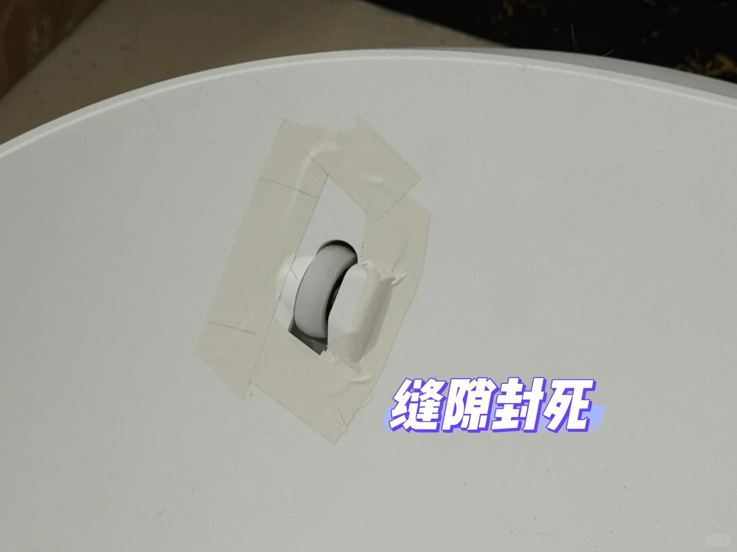 Close-up of a small support roller in the white litter-box base, with light tape around the roller opening and a Chinese text overlay.