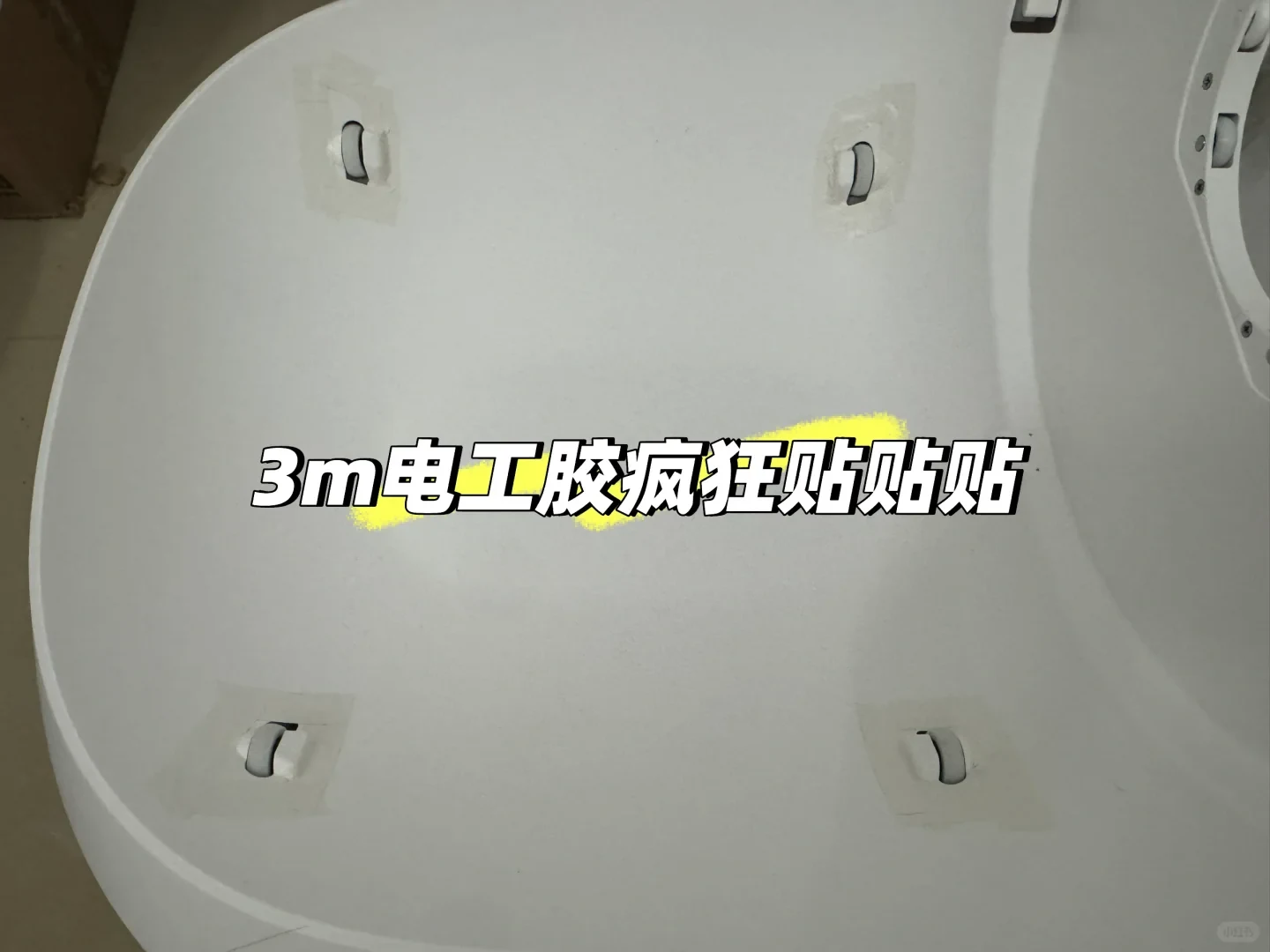 Top-down view of the interior base of a white plastic machine, likely a smart pet litter box or rotating drum device, with four embedded small rollers each taped down along their edges with strips of white tape. Across the center is Chinese text with a yellow highlight.