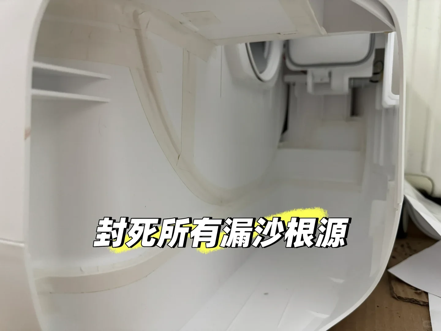 Interior view of a white plastic automatic cat litter box chassis where seams and gaps have been sealed with white tape, overlaid with bold Chinese text.