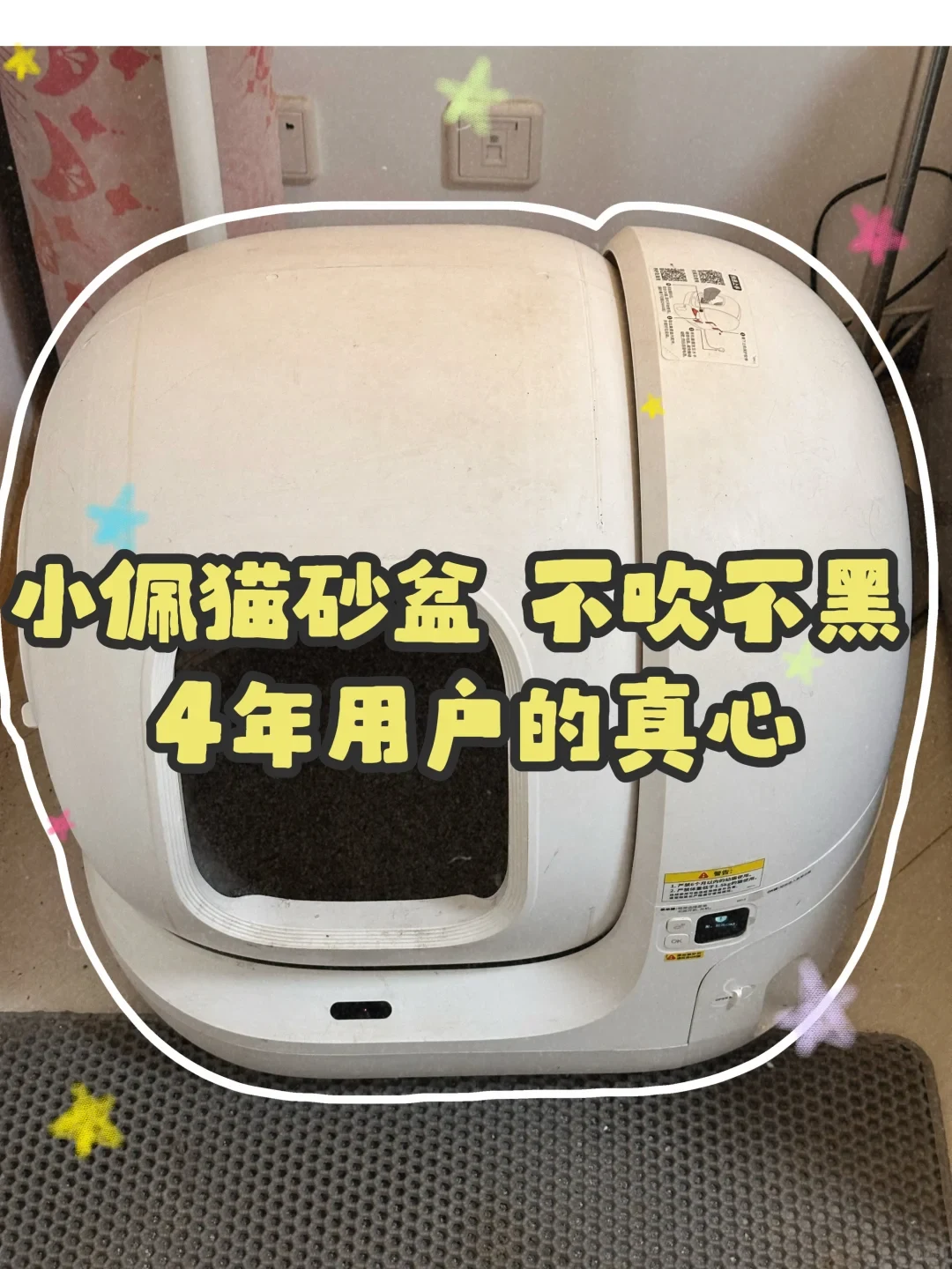 A front view of a white PETKIT automatic cat litter box placed on a grey litter mat indoors, overlaid with large yellow Chinese text across the front opening.