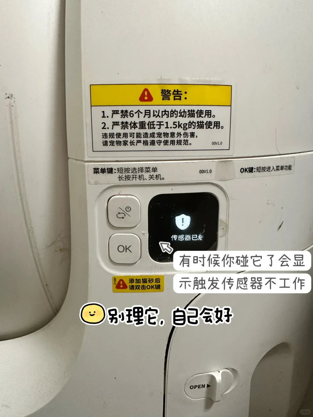 Close-up of the control panel on a white Petkit automatic cat litter box, showing an OK button, a power/menu button, warning labels, and a digital screen displaying a shield exclamation mark icon with sensor triggered text.