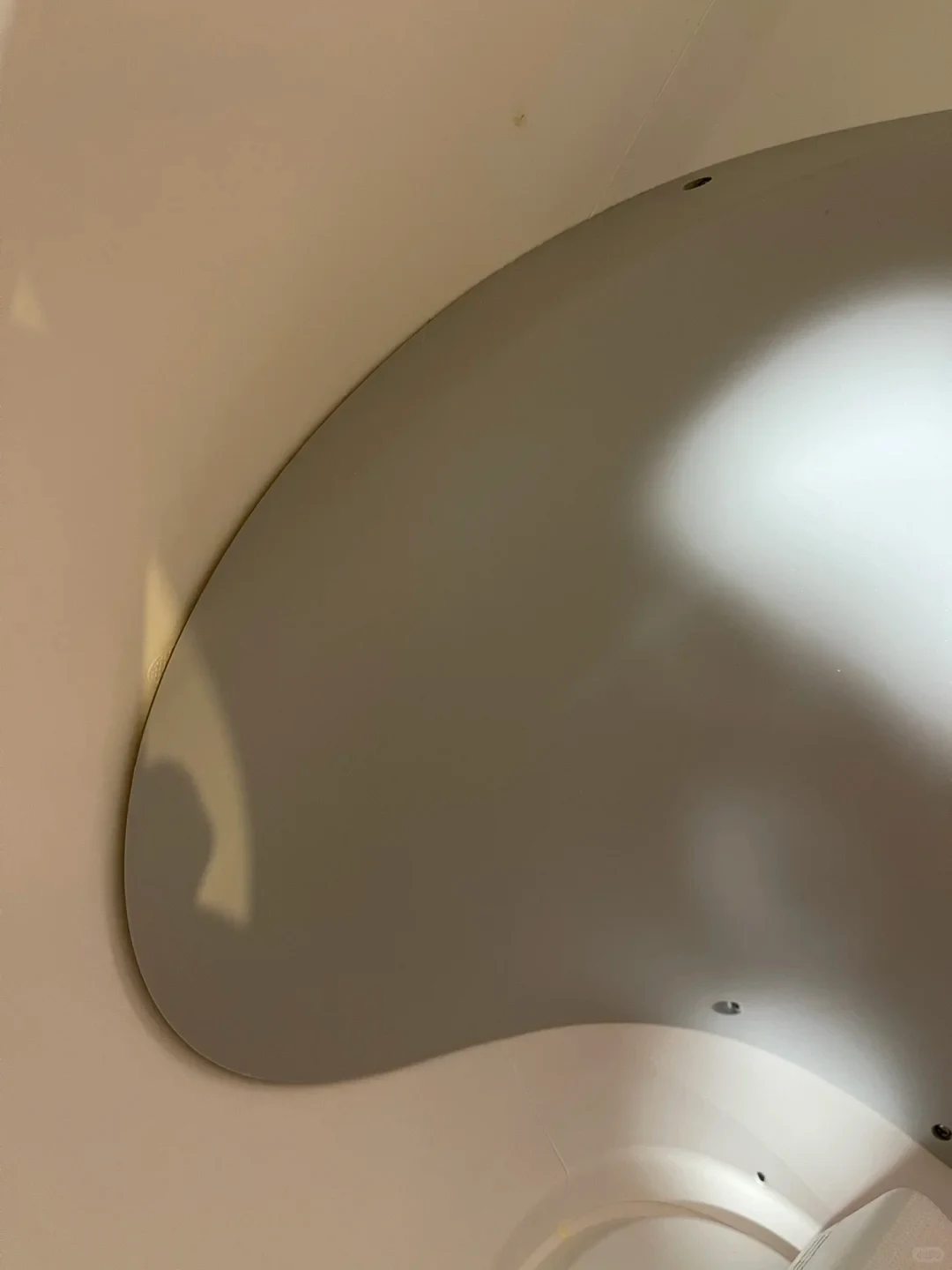 A close-up view of interior curved surfaces, showing a smooth, light gray curved panel fitted against an off-white wall with subtle lighting reflections and small screw holes along the edges.