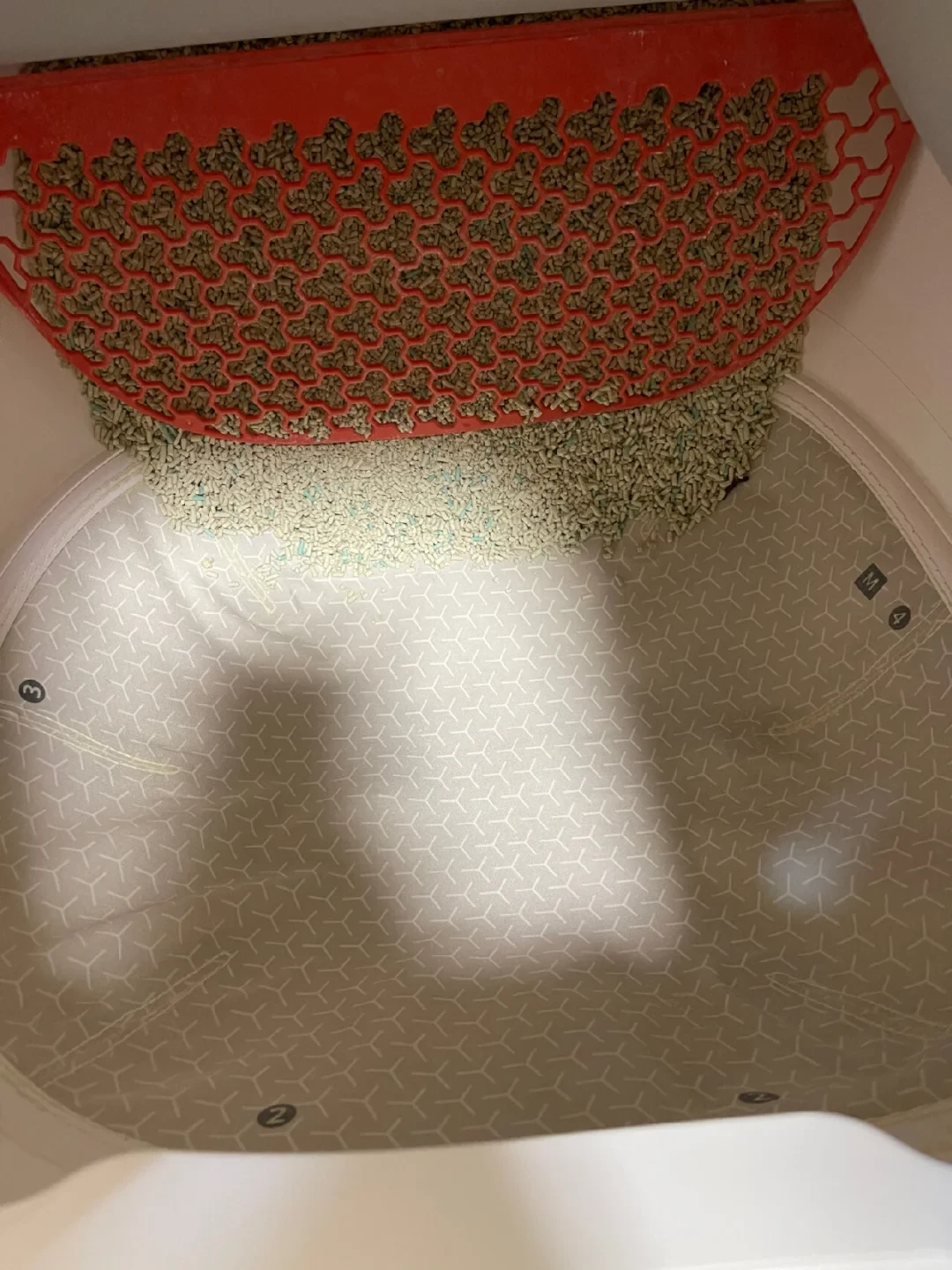 An overhead view into the interior drum of an automatic self-cleaning cat litter box, showing an empty patterned liner with numbered markers along the rim and pellet litter partially sifted above a curved red grate at the top.
