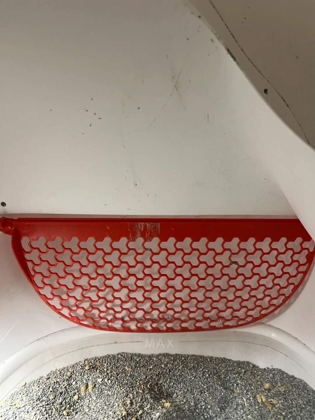 Interior view of an automatic litter box featuring a curved red sifting grate mounted above a tray filled with gray cat litter and marked with an embossed MAX line.
