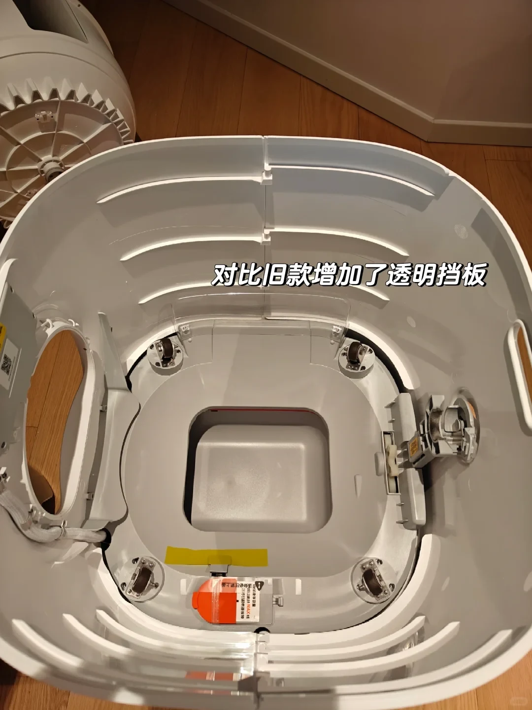 Top-down view into the interior chassis of an automatic cat litter box, displaying internal rollers, central waste chute, and a curved transparent baffle attached along the back curved wall.