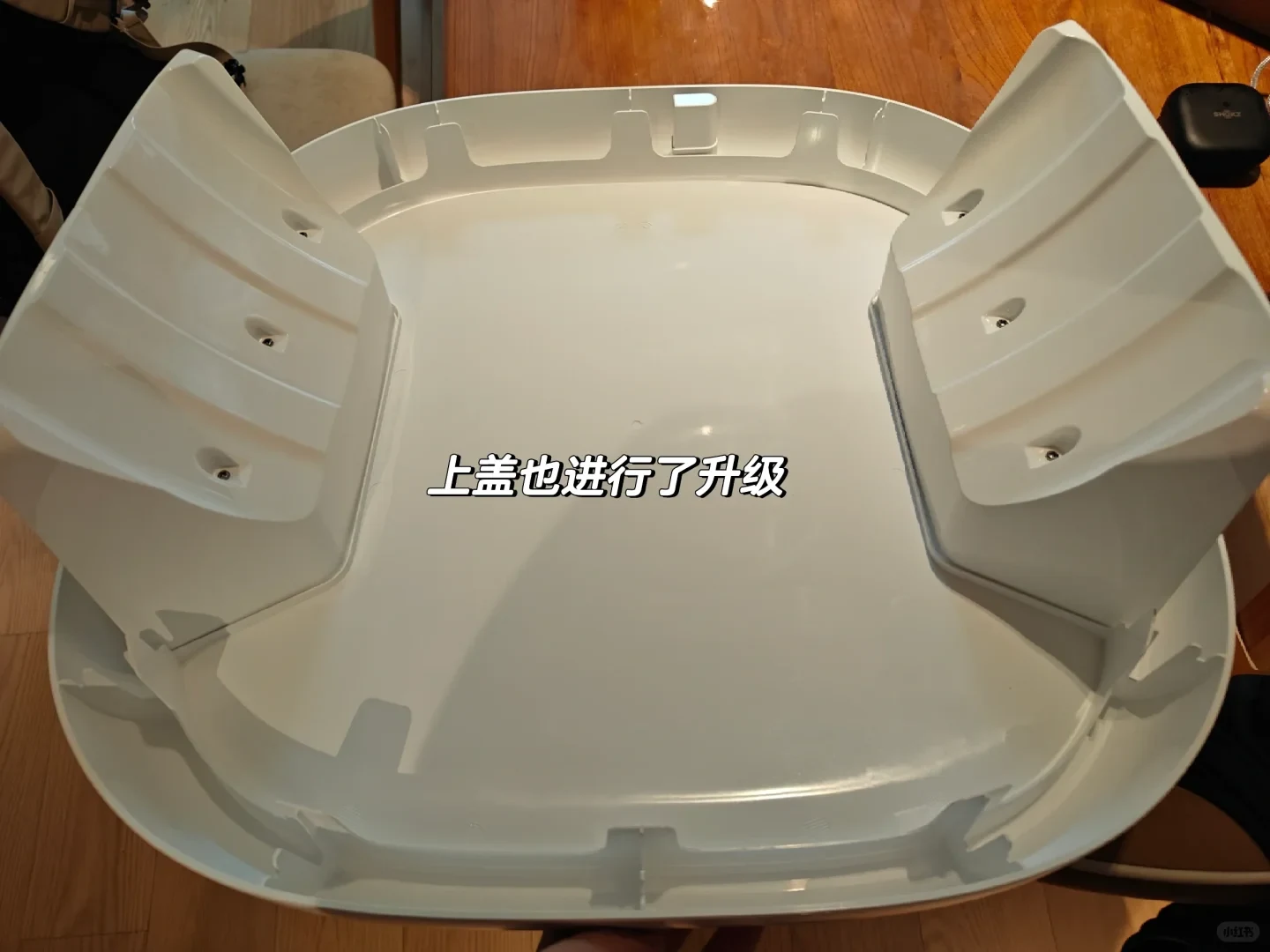 Interior view of a white plastic top cover for a pet appliance, featuring two raised side sections on a rounded rectangular base, resting on a wooden surface.