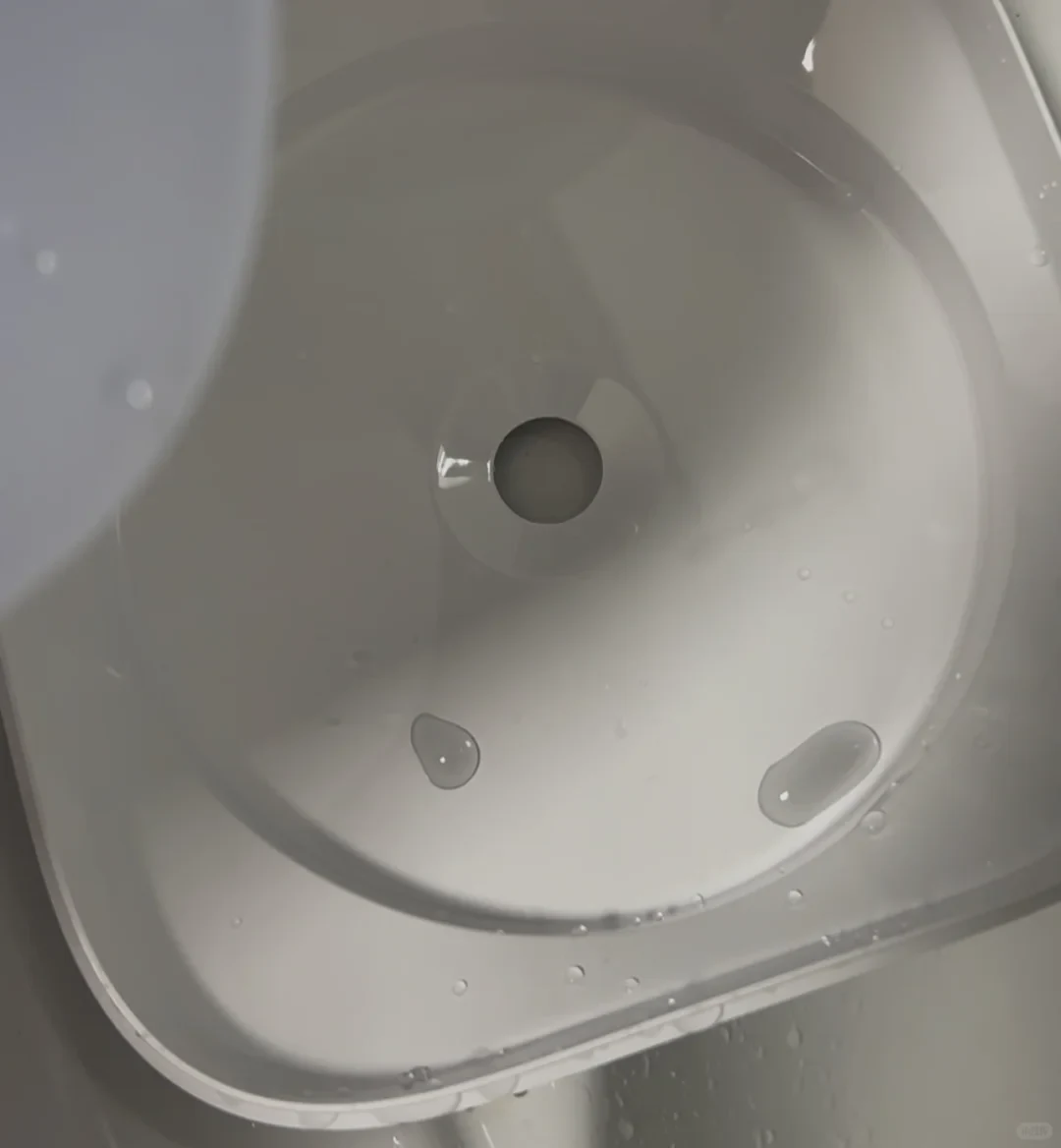 Top-down view of a white plastic container basin with water droplets gathered around a central drain hole.