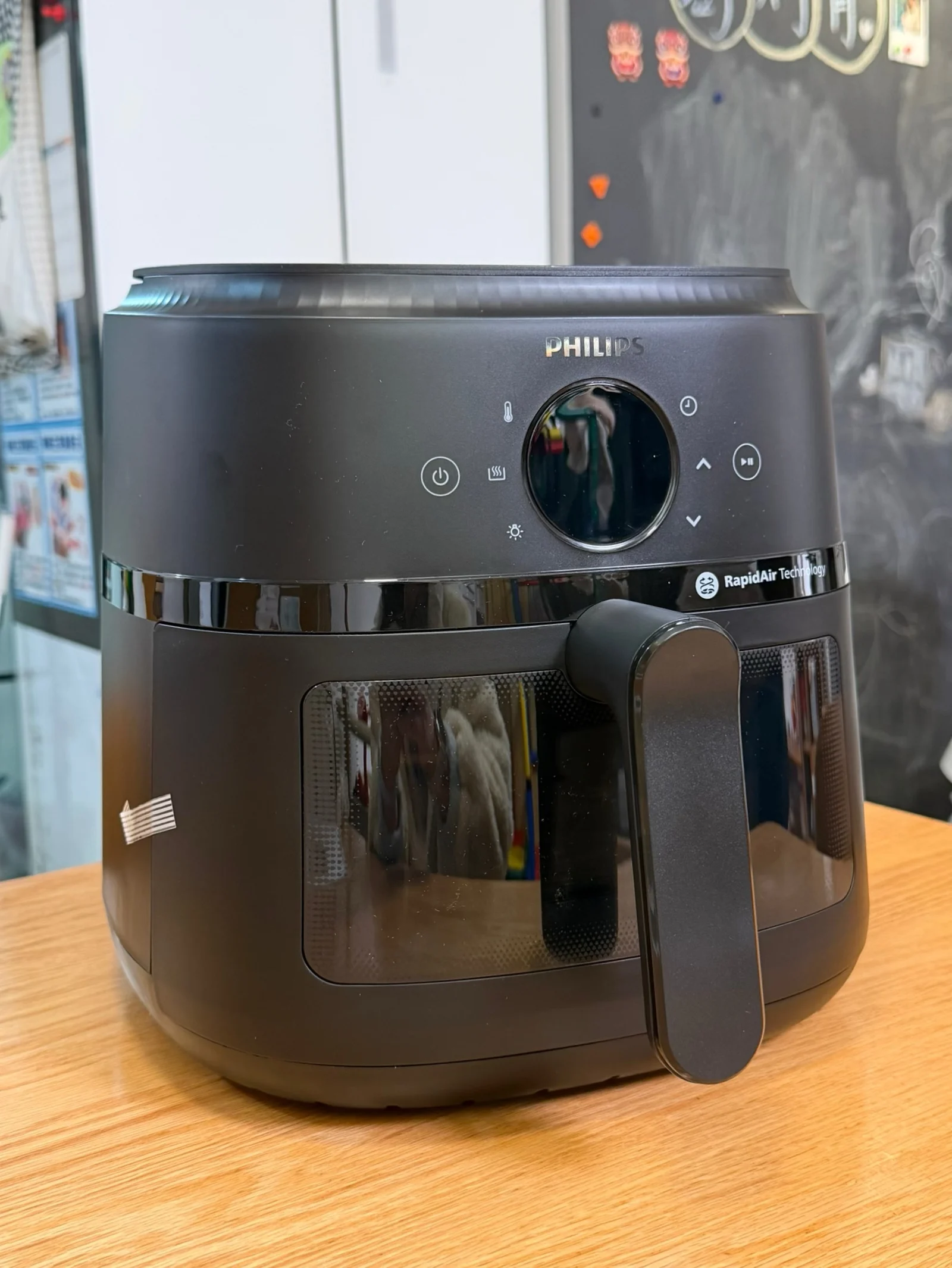 A Philips NA230 air fryer on a wooden table, with its handle and viewing window visible.