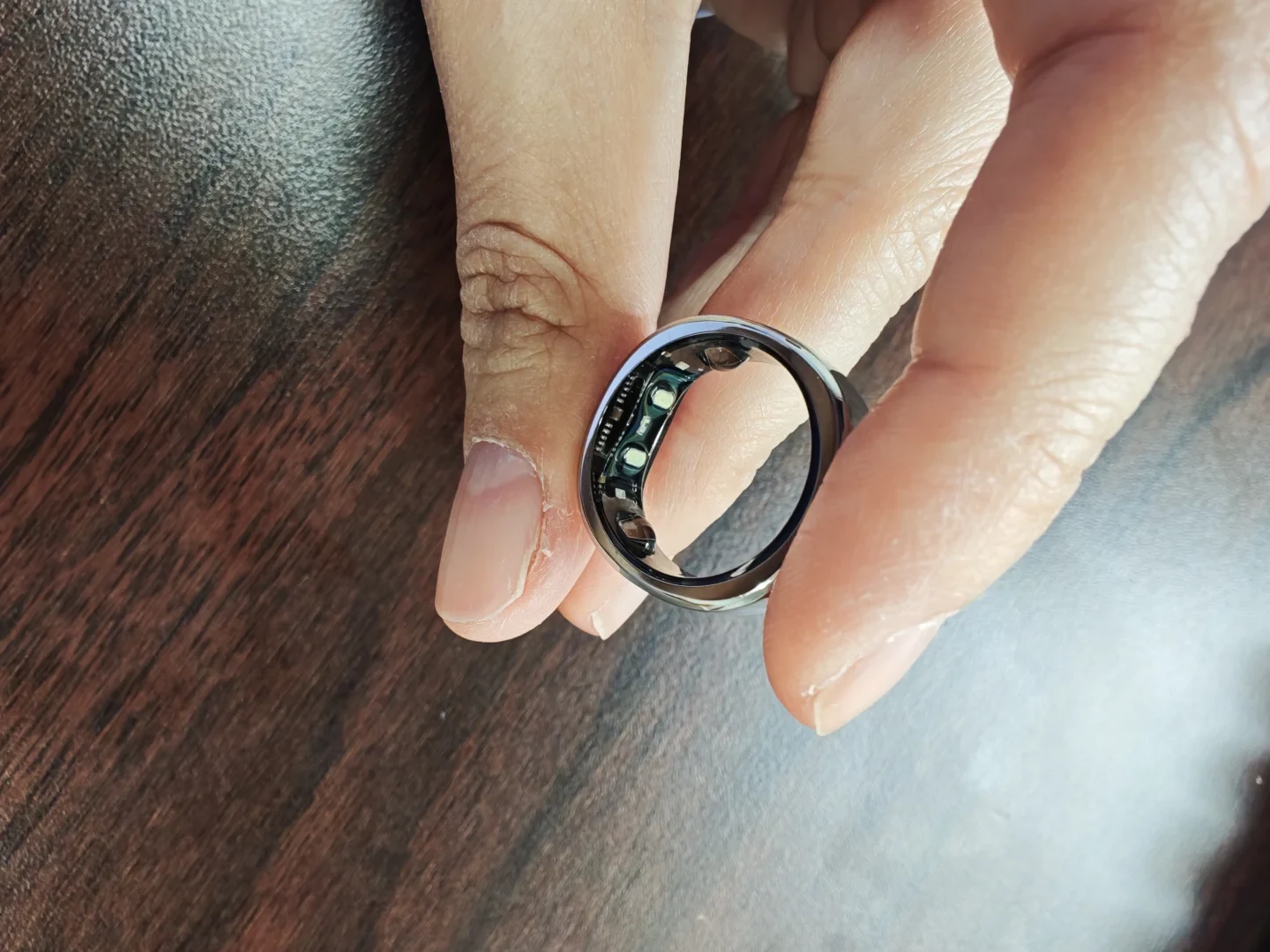 A person holding a silver smart ring between their fingers, showing the interior sensors and electronic circuitry.