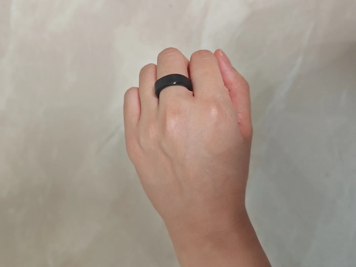 A person wearing a wide black smart ring on their index finger against a plain beige background.