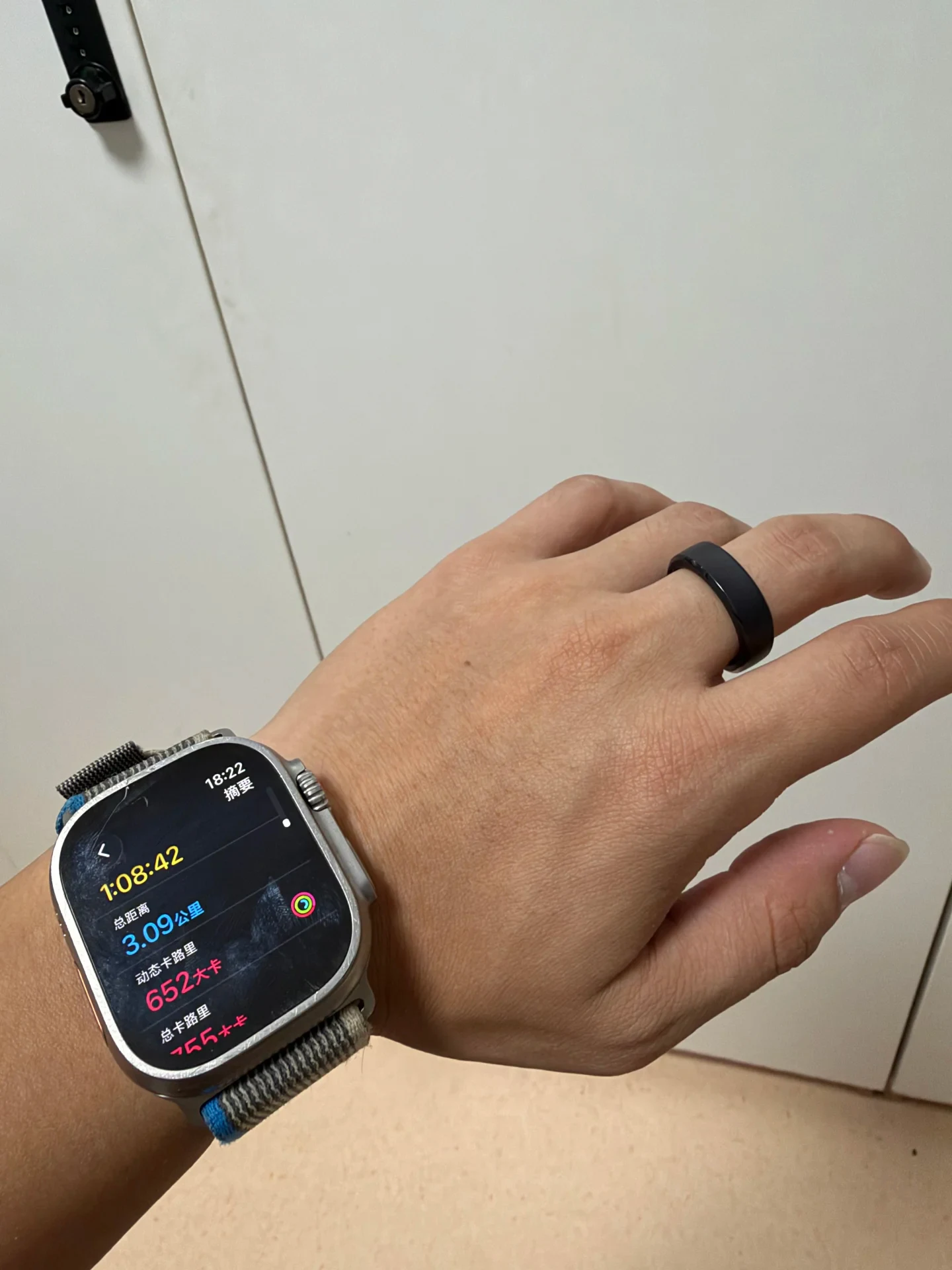 A person's hand wearing a black smart ring on the ring finger and an Apple Watch Ultra on the wrist displaying a workout summary.