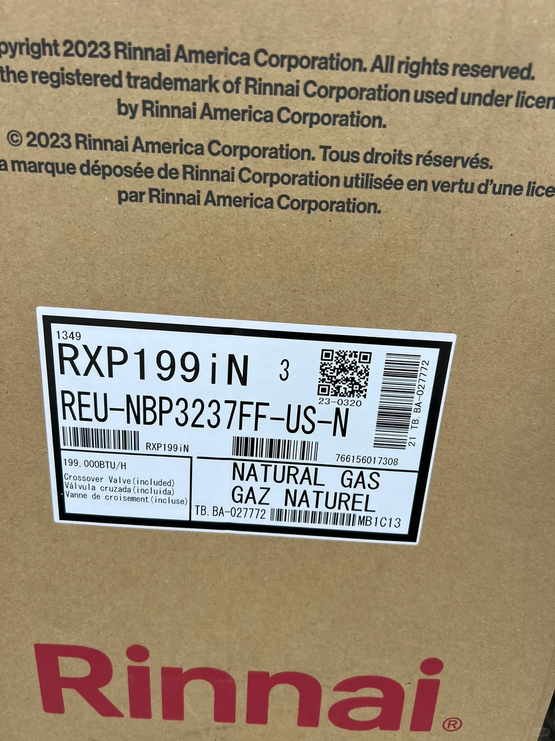 Close-up of a Rinnai cardboard appliance box with a product label for model RXP199 iN, marked natural gas and 199,000 BTU/h, with barcodes and a QR code.