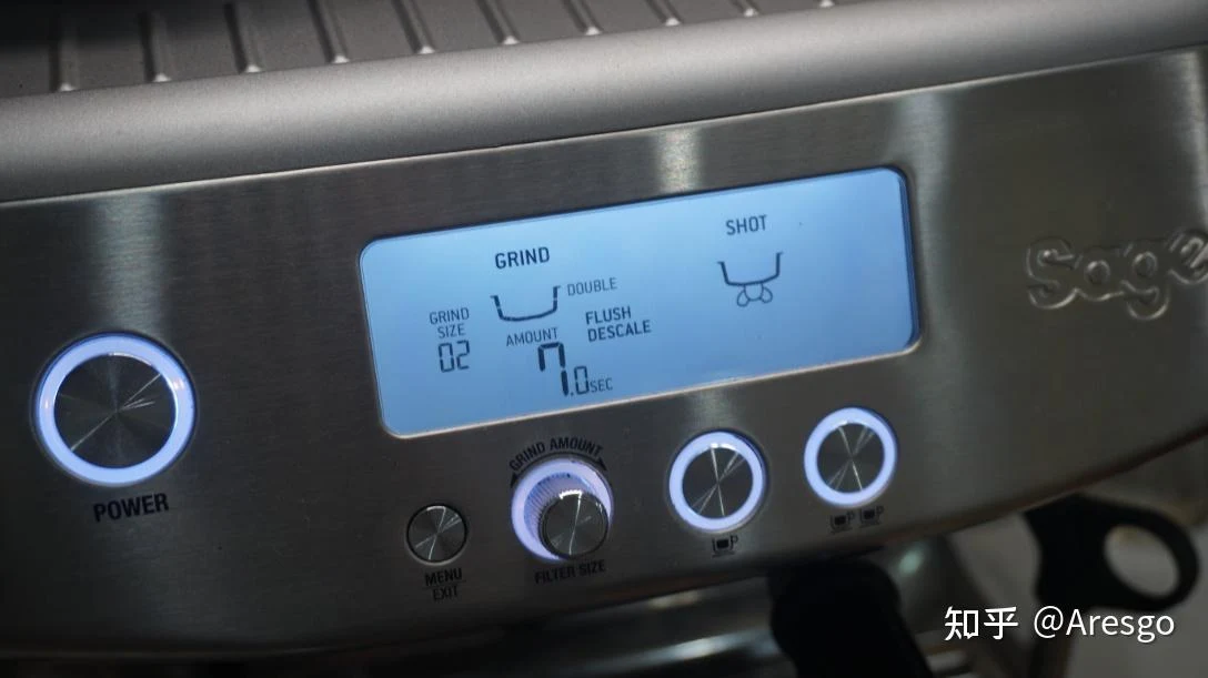 Close-up of the stainless-steel Sage espresso machine control panel, showing a blue display with grind size 02, grind amount 7.0 seconds, and a double-shot setting, with illuminated power, menu, grind-amount, and single- and double-shot buttons.
