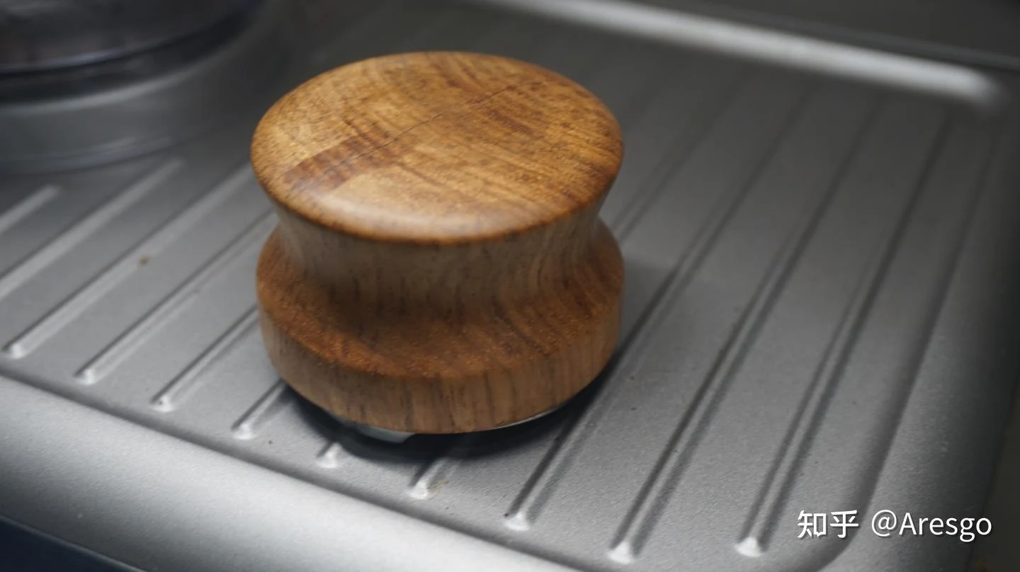 A round wooden coffee distribution tool rests on the stainless-steel drip tray of an espresso machine.