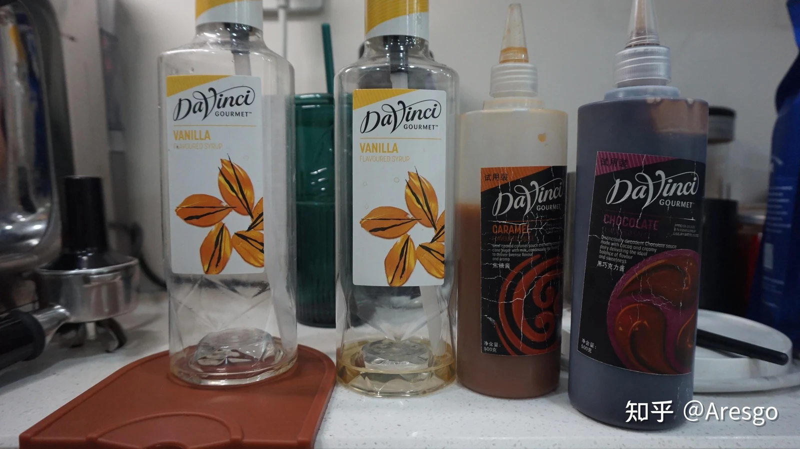 Four bottles of DaVinci Gourmet syrups and sauces on a kitchen counter, including two tall bottles of vanilla syrup and two squeeze bottles of caramel and chocolate sauce.