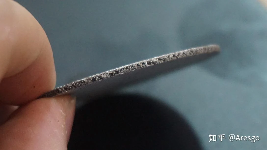 Close-up of fingers holding a sintered metal espresso puck screen, showing its porous edge profile.