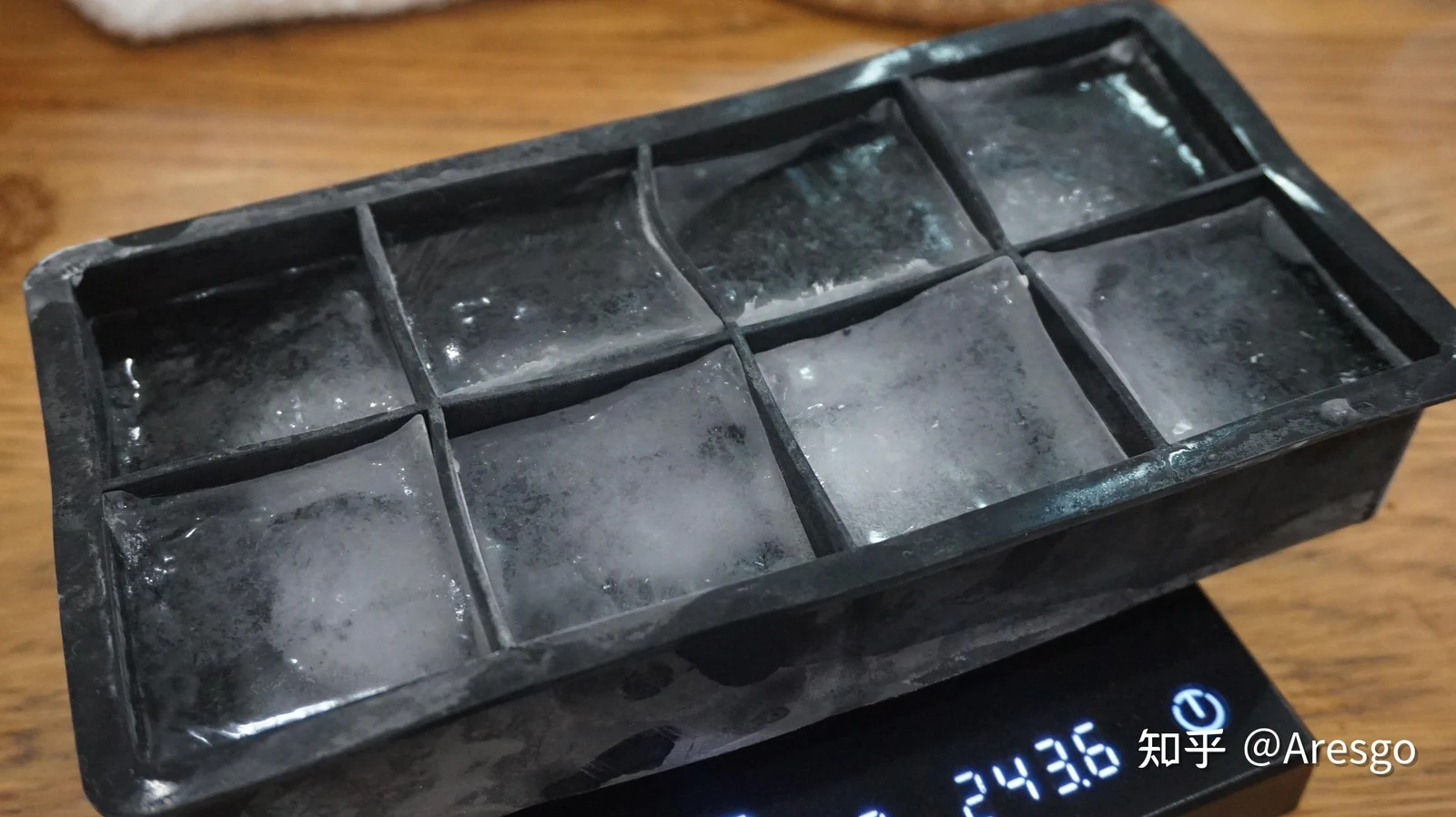 A black silicone ice cube tray filled with eight large frozen ice cubes resting on a digital scale.