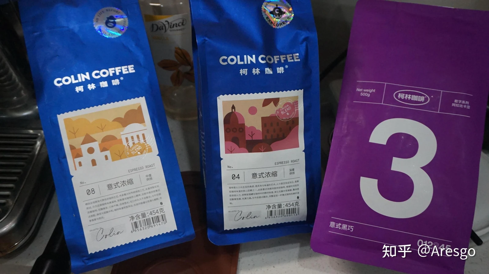 Three bags of Colin Coffee beans lined up on a kitchen counter next to an espresso machine