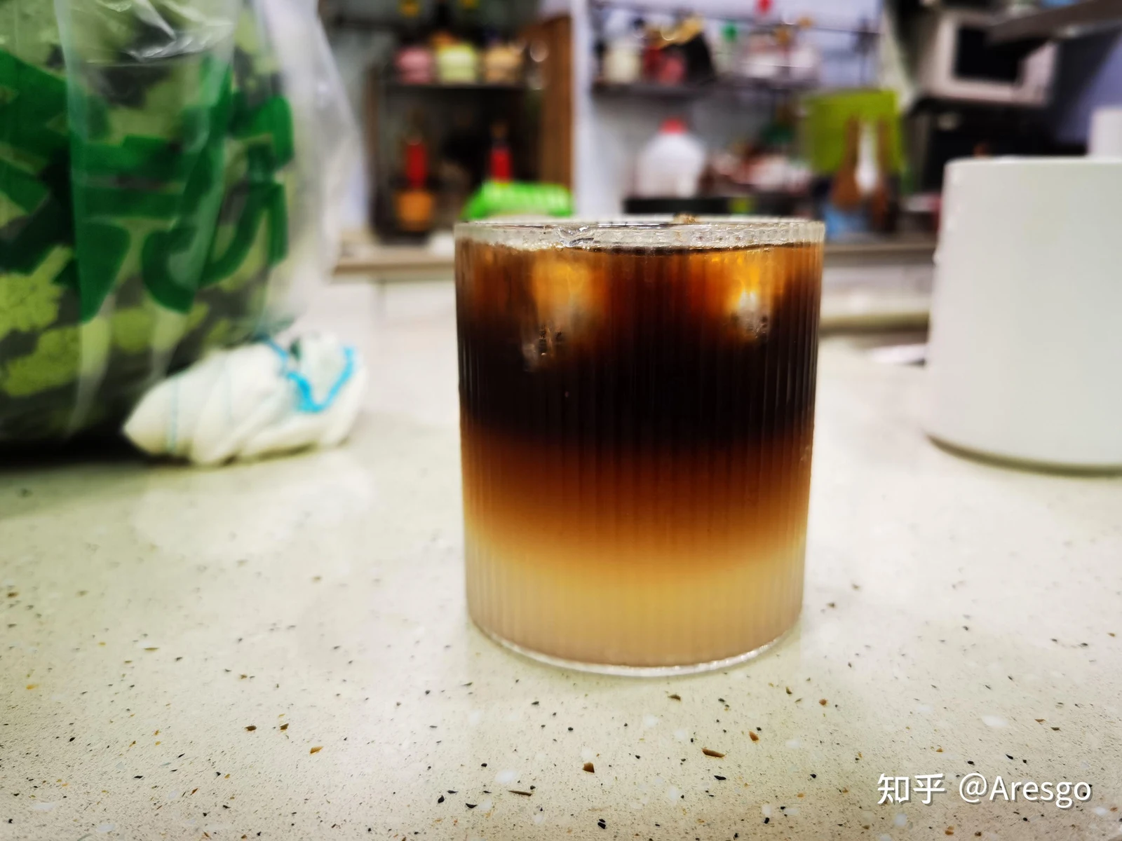 Layered iced coconut black coffee in a ribbed glass on a kitchen countertop