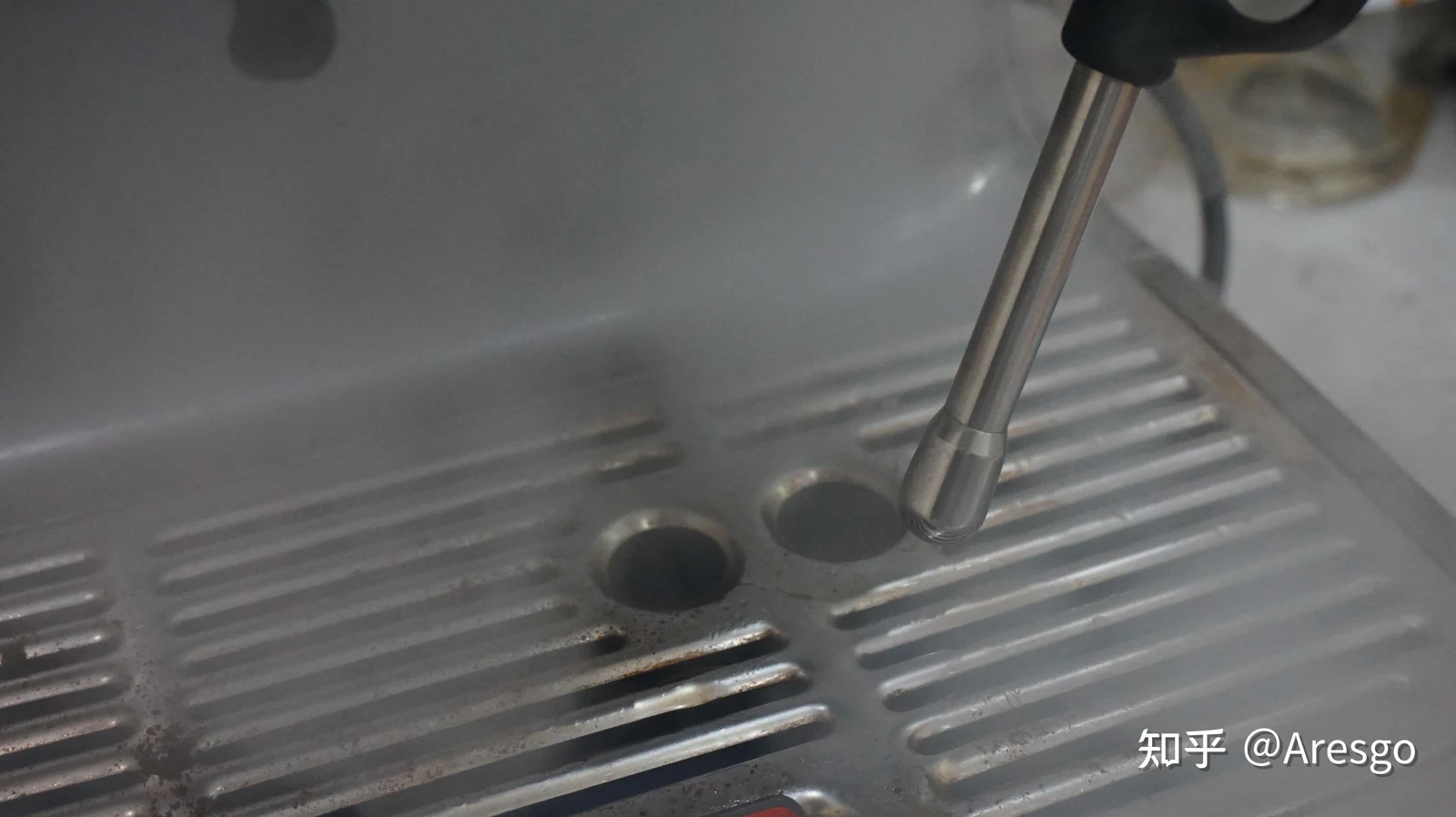 Close-up of the steam wand tip emitting steam over the metal drip tray grate of the Sage 878 espresso machine.
