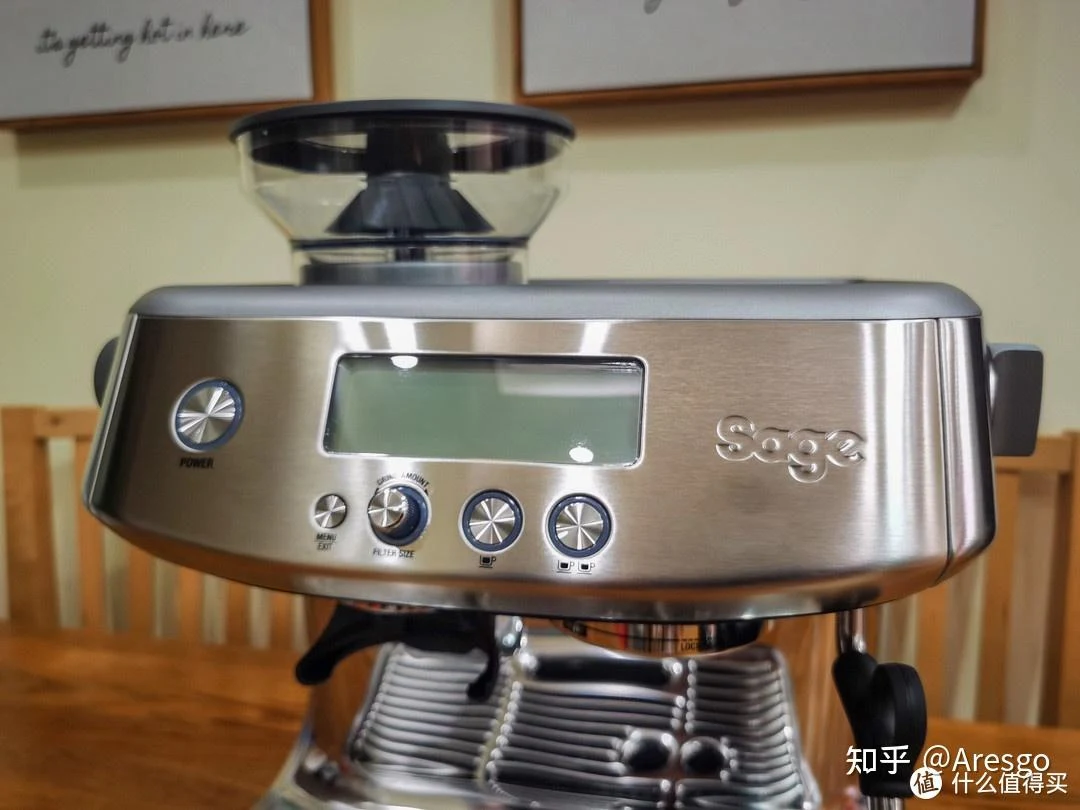 Front view of a stainless-steel Sage espresso machine with an integrated grinder and bean hopper, showing a display, control knobs, buttons, portafilter, and drip tray.
