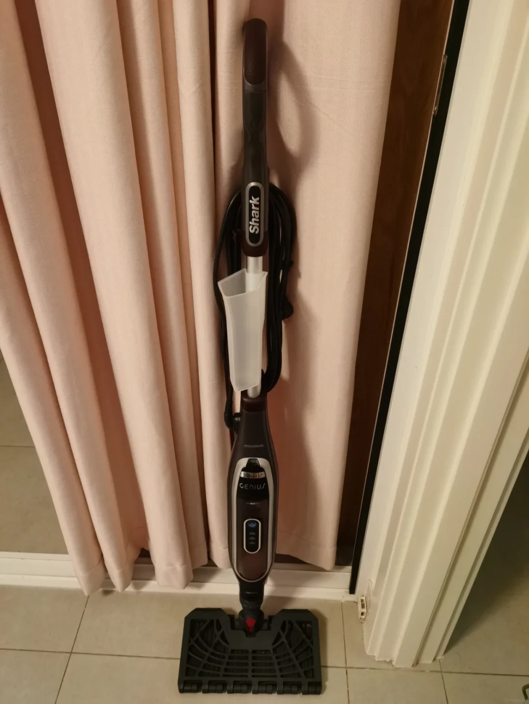 Shark Genius steam mop leaning vertically against a curtain indoors.