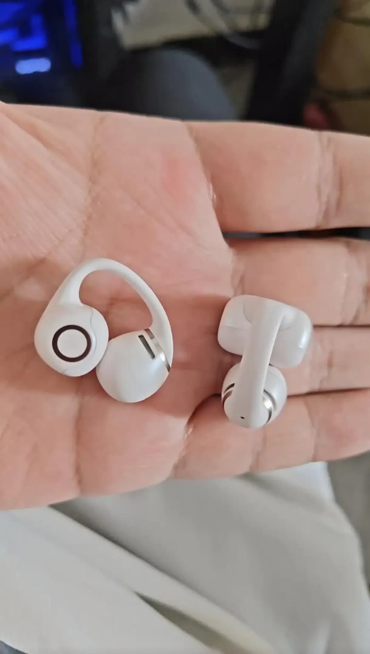 A close-up shot of two white clip-on open-ear earbuds resting side-by-side on an open palm.