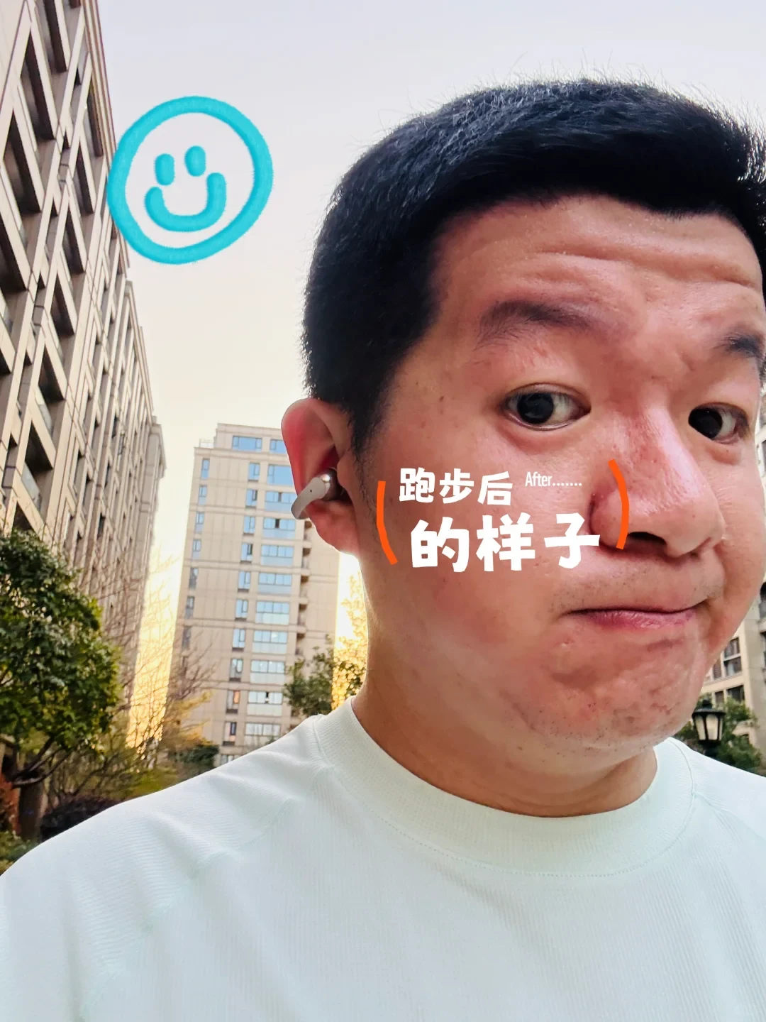 A close-up selfie of a man outdoors with flushed skin and sweat after a run, wearing an open-ear sports headphone on his ear. Residential apartment buildings are visible in the background, along with a teal drawn smiley face in the upper left.