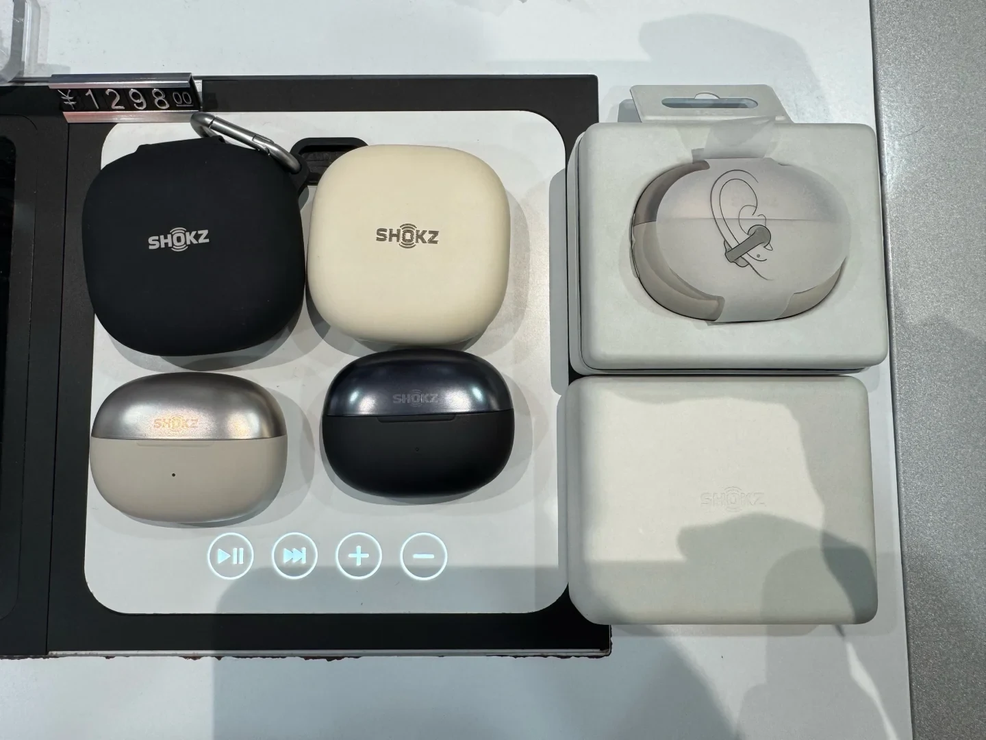 A retail demonstration display included in the source post, with Shokz earbud charging cases, an ear-hook demo unit and a price label.