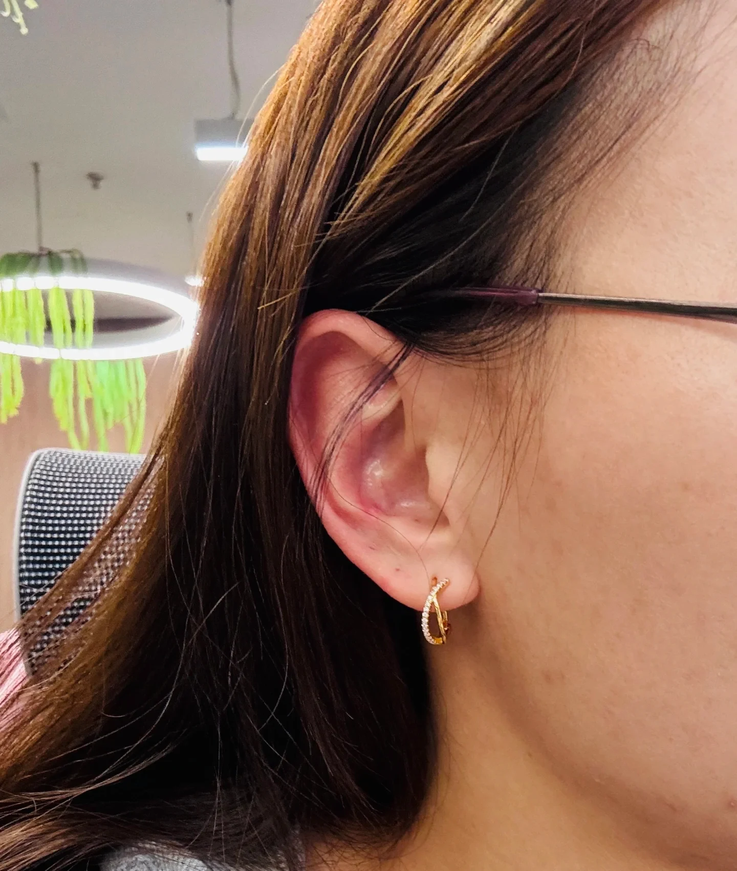 Close-up profile of a person's right ear showing noticeable redness along the outer cartilage and concha, with a small gold hoop earring and eyeglass temple visible.