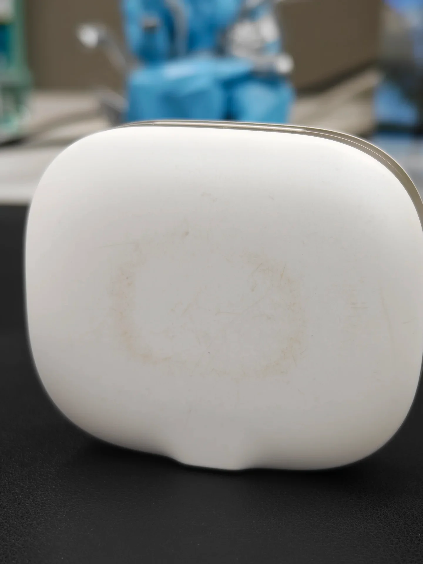 Close-up of the white matte charging case showing faint circular scuff marks and discoloration on the surface.