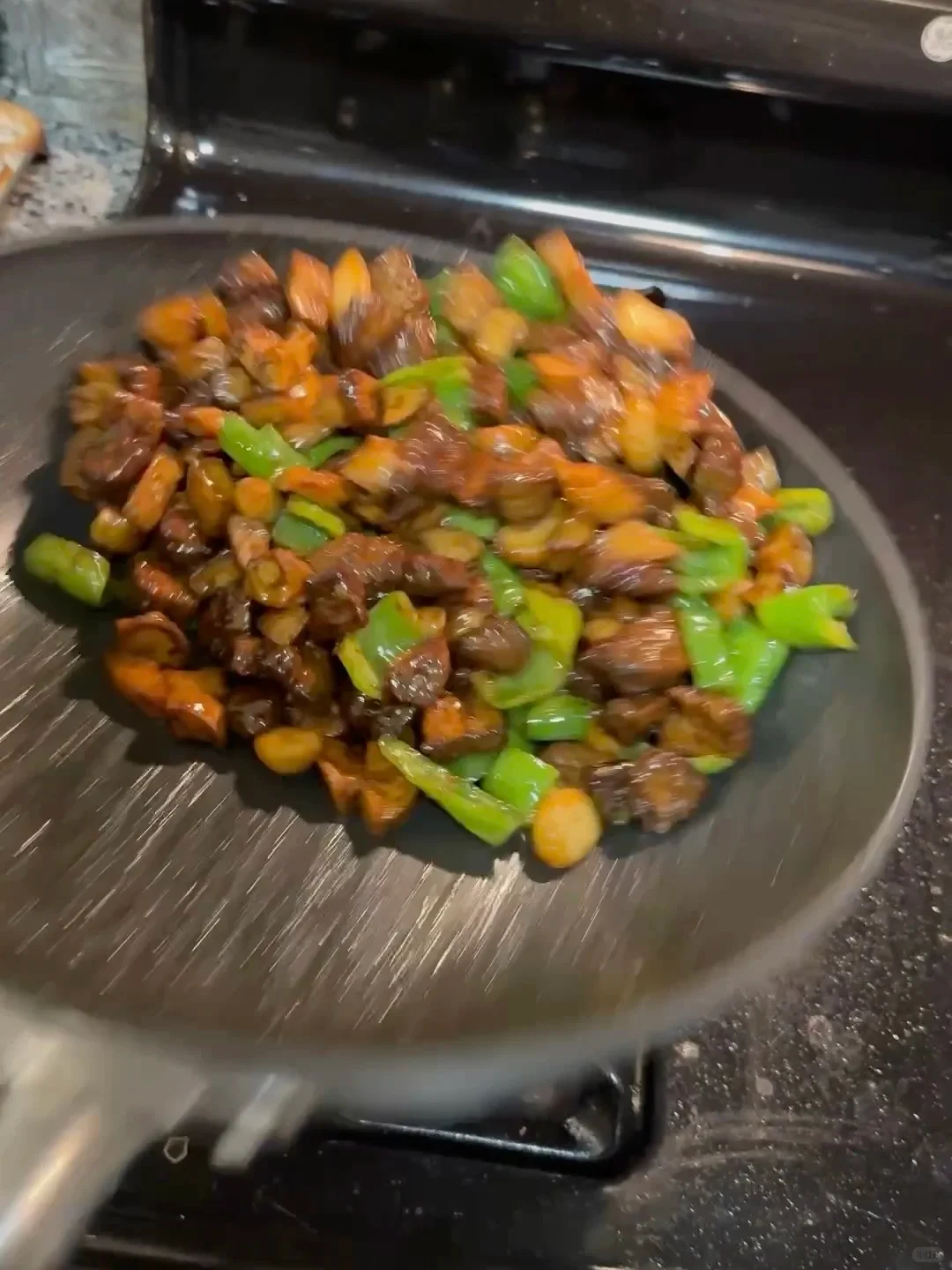 A frying pan on a stovetop holds a glossy stir-fry of browned meat, orange pieces, and green pepper.