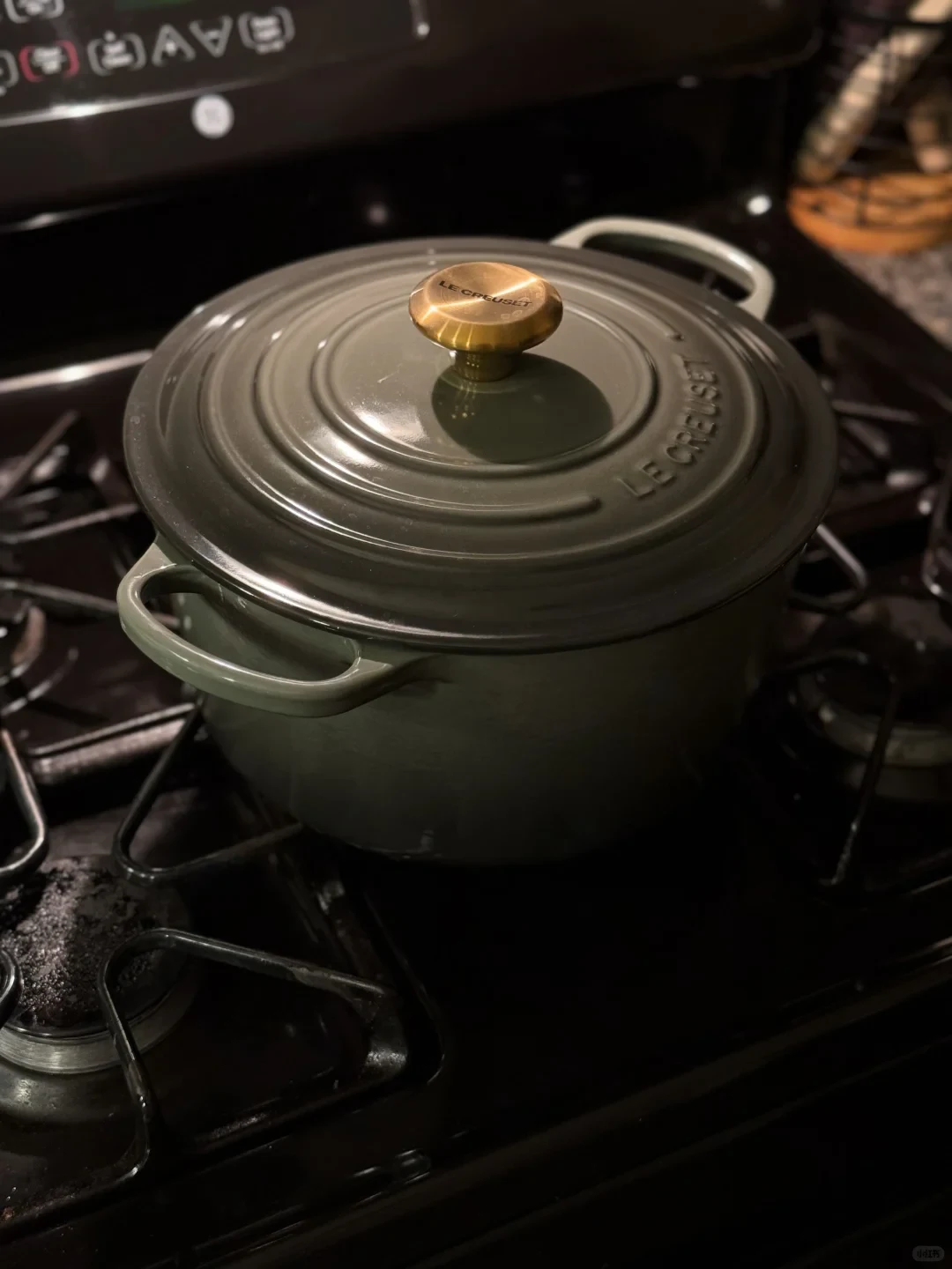 A dark olive-green Le Creuset pot with a ridged lid and gold knob sits on a gas stovetop.