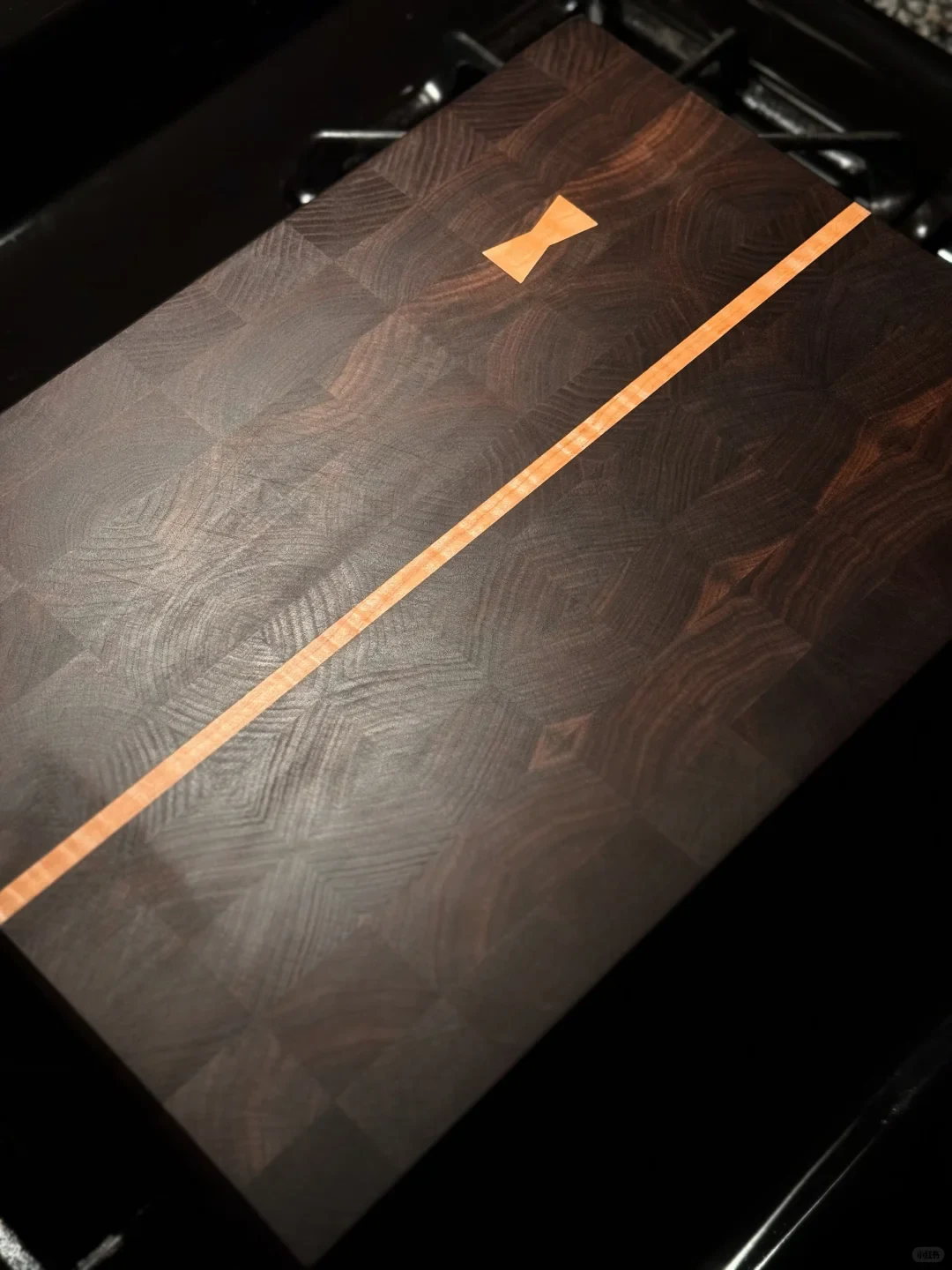 A dark end-grain cutting board with a light wood stripe and bow-tie inlay rests on the kitchen counter.