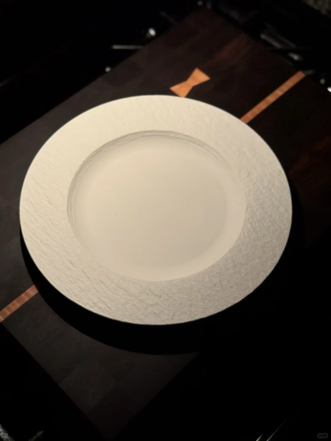 A white, broad-rimmed textured plate rests on the dark wooden cutting board with its light-colored inlay visible beneath.