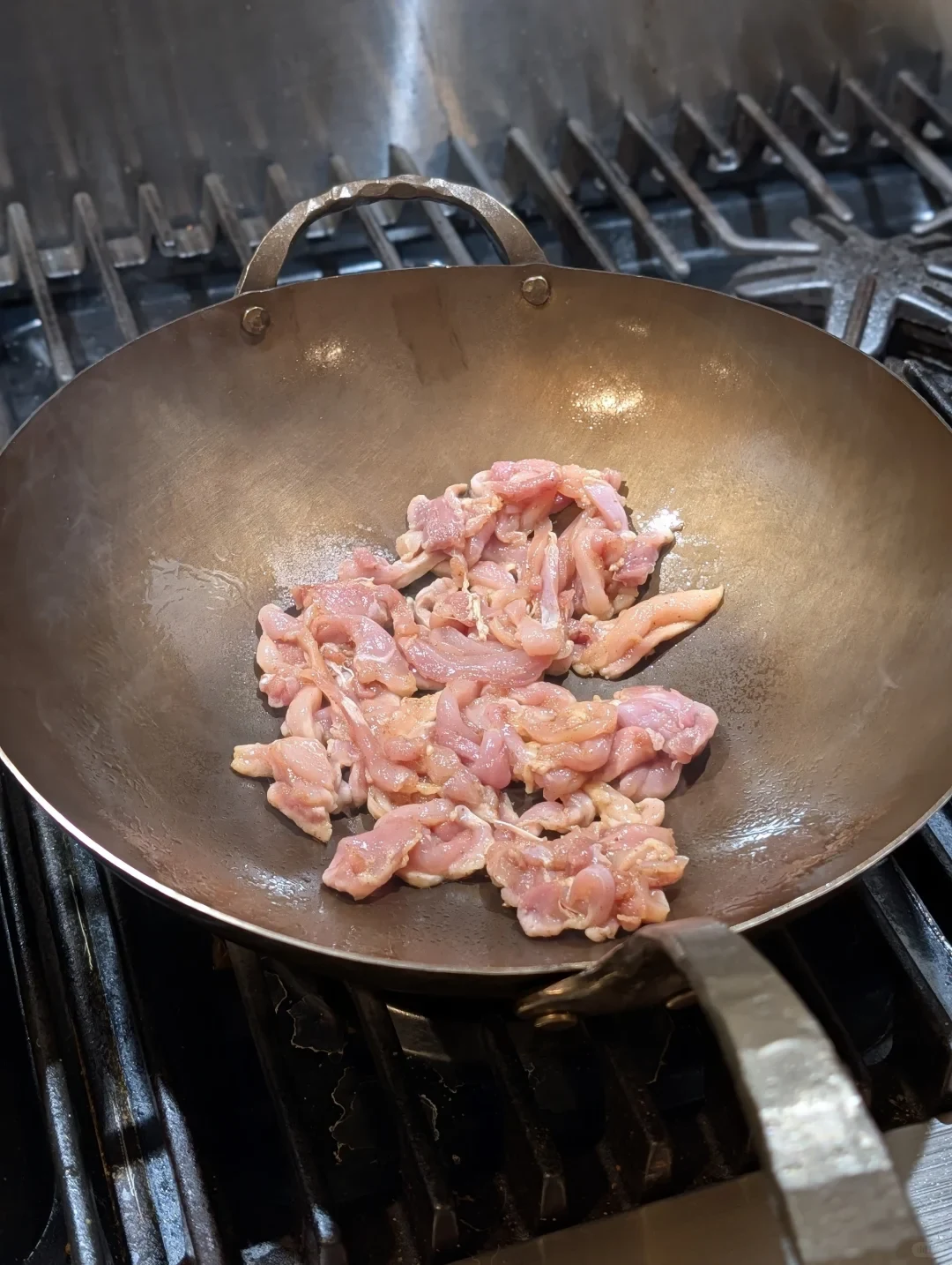 Pieces of raw pink meat sit in a large metal wok on a gas stove.