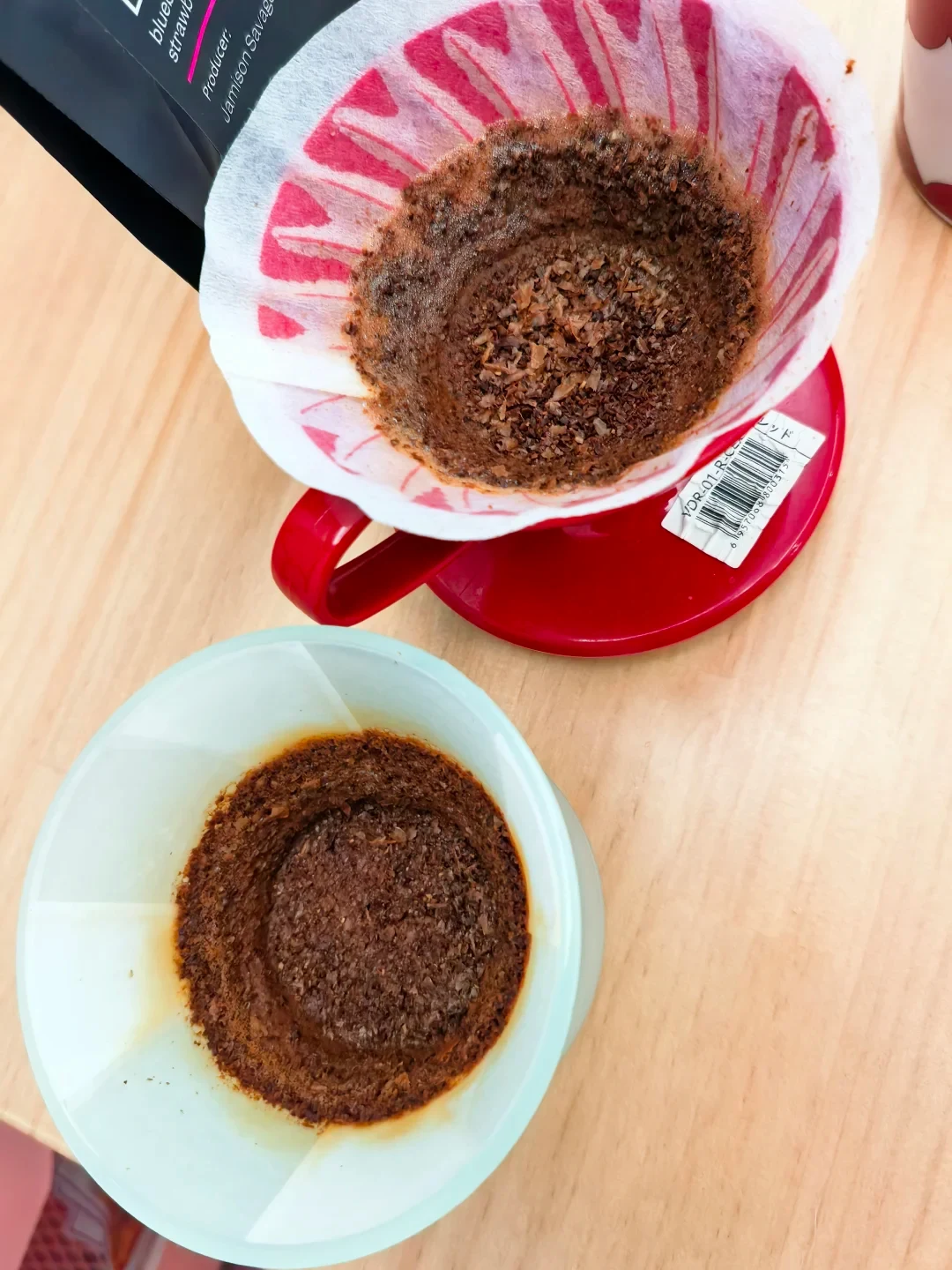 Used paper filters and coffee grounds sit in a red HARIO V60 above and a pale translucent SOLO dripper below. Both coffee beds and the paper against each dripper wall are visible.