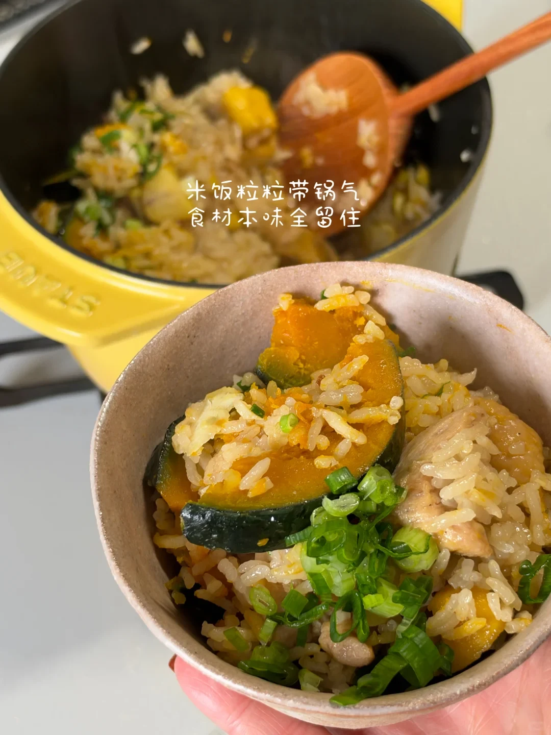 A bowl of pumpkin and chicken cooked rice topped with chopped scallions, held in hand in front of a yellow cast-iron pot containing the rest of the dish.