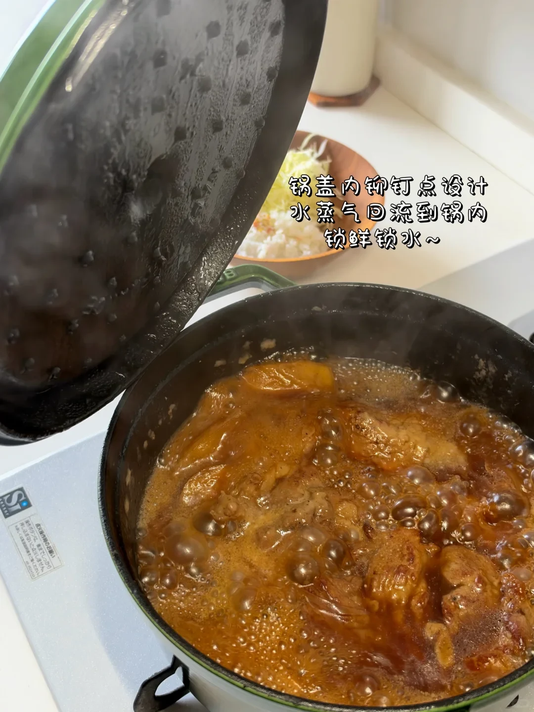 A green cast iron Dutch oven on a stovetop with its lid lifted, showing food simmering in a bubbly, savory brown sauce while condensed steam coats the studded underside of the lid.