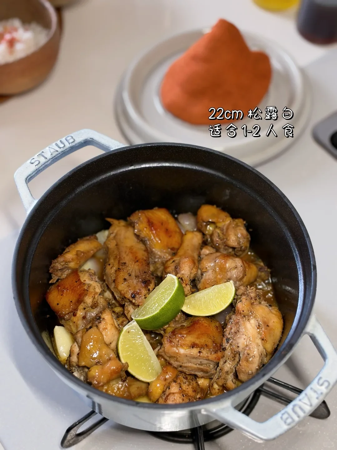 Chicken pieces with lime wedges inside a STAUB cocotte on a stovetop.