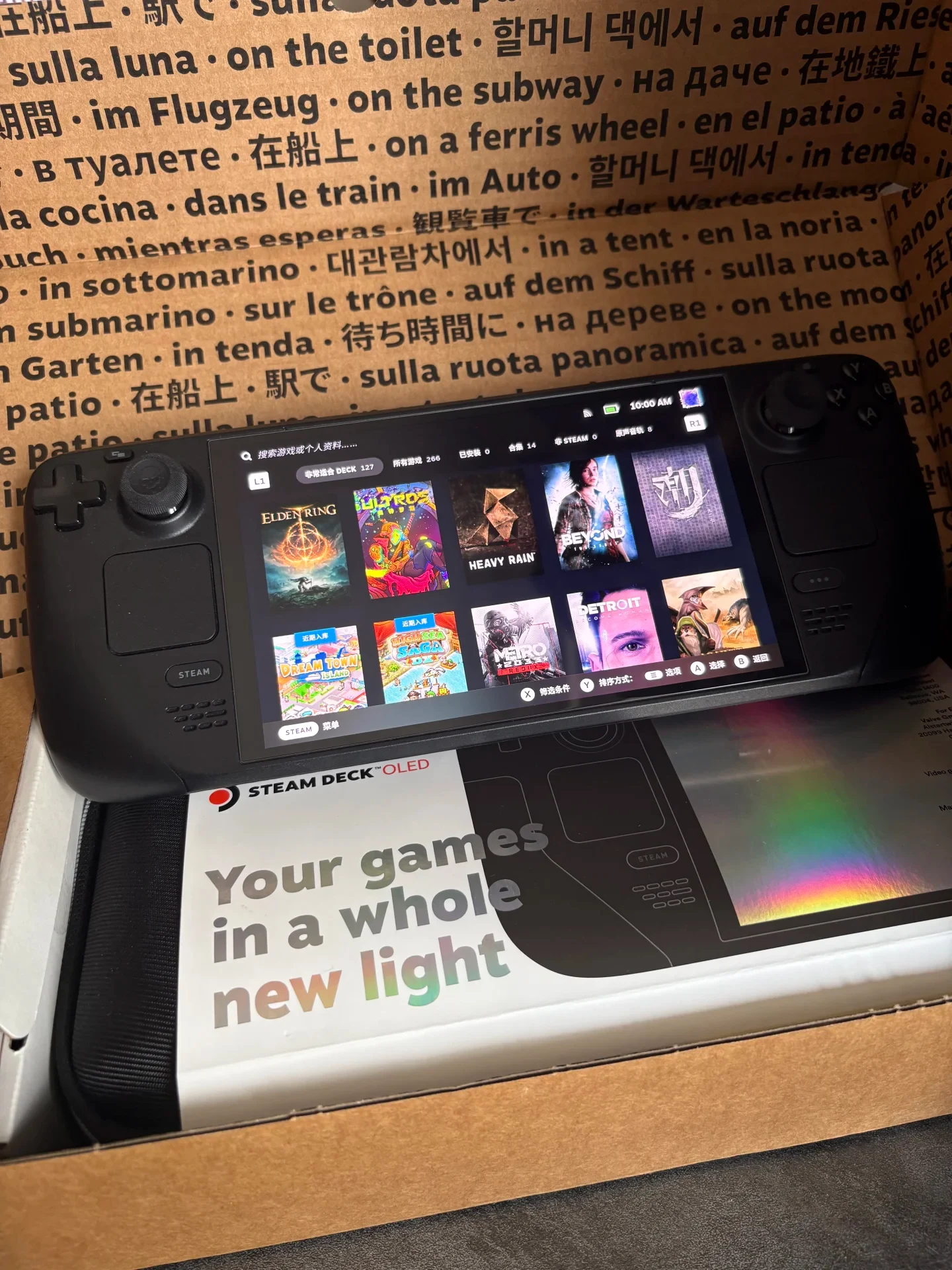 A Steam Deck handheld console resting inside its cardboard unboxing packaging with the system powered on, displaying the Steam game library menu.