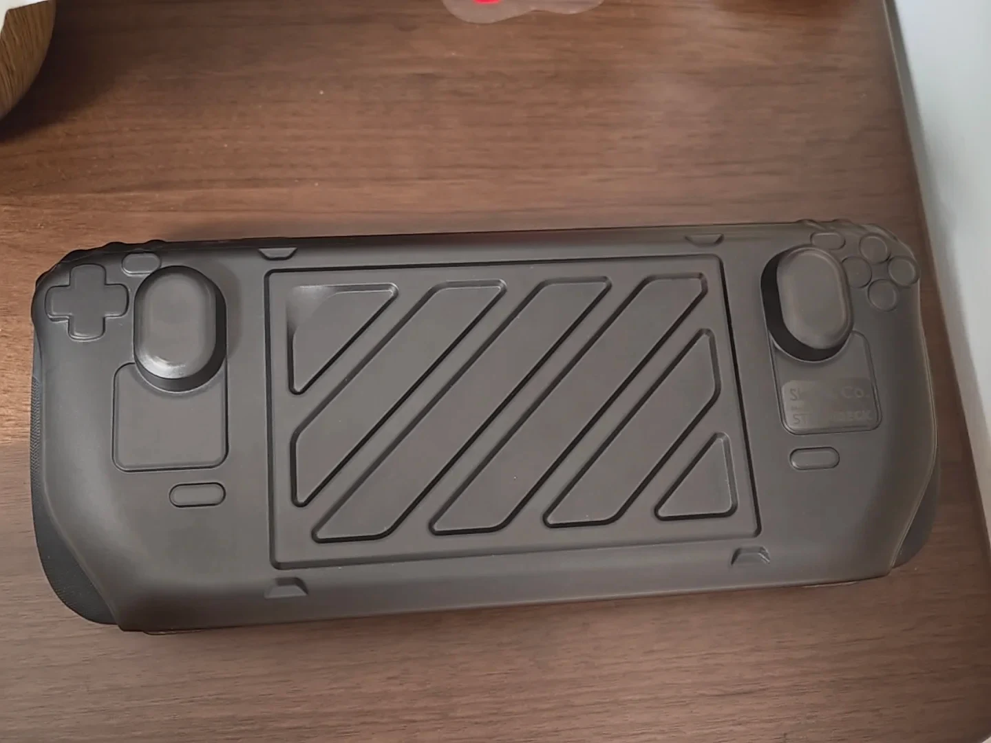A black Steam Deck handheld console fitted with a protective hard front cover, lying horizontally on a wooden surface.